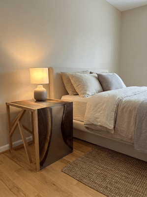 Bedroom with a neatly made bed, nightstand with a lamp, and a beige rug on hardwood floor.