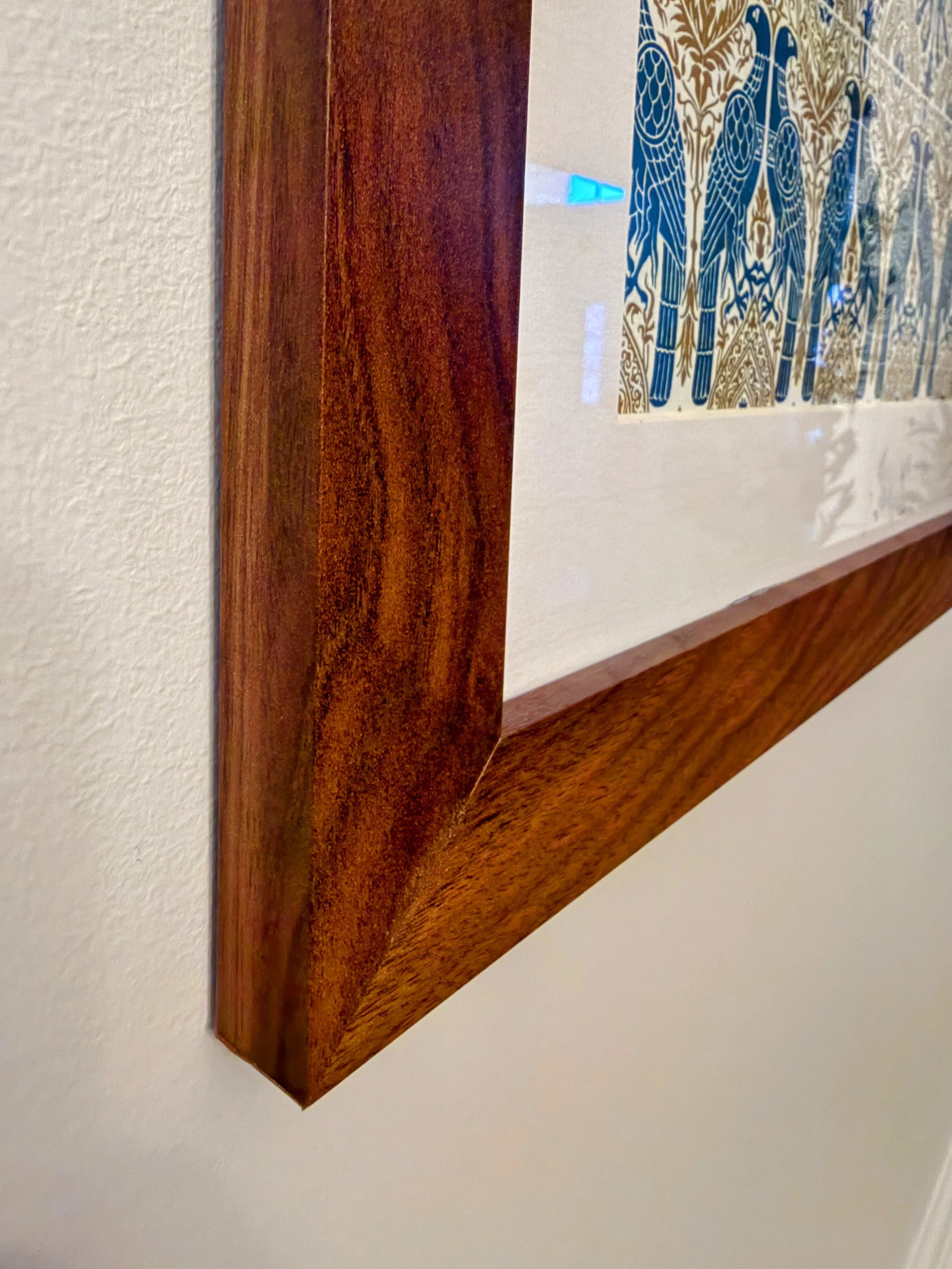 Close-up of a wooden picture frame mounted on a white wall, with a section of artwork visible inside the frame.