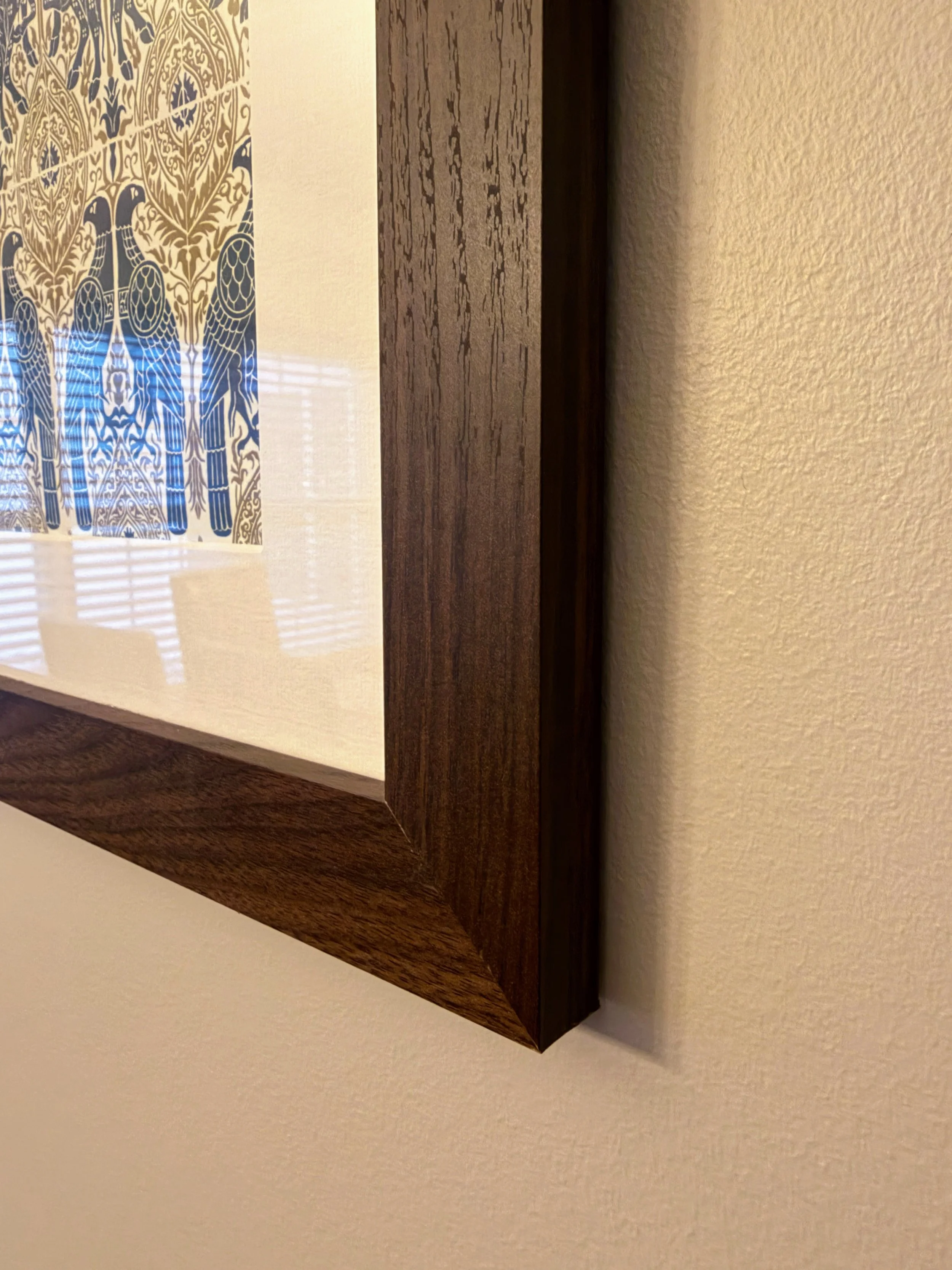 Close-up of a wooden picture frame corner hanging on a beige wall, with a partial view of artwork inside the frame.