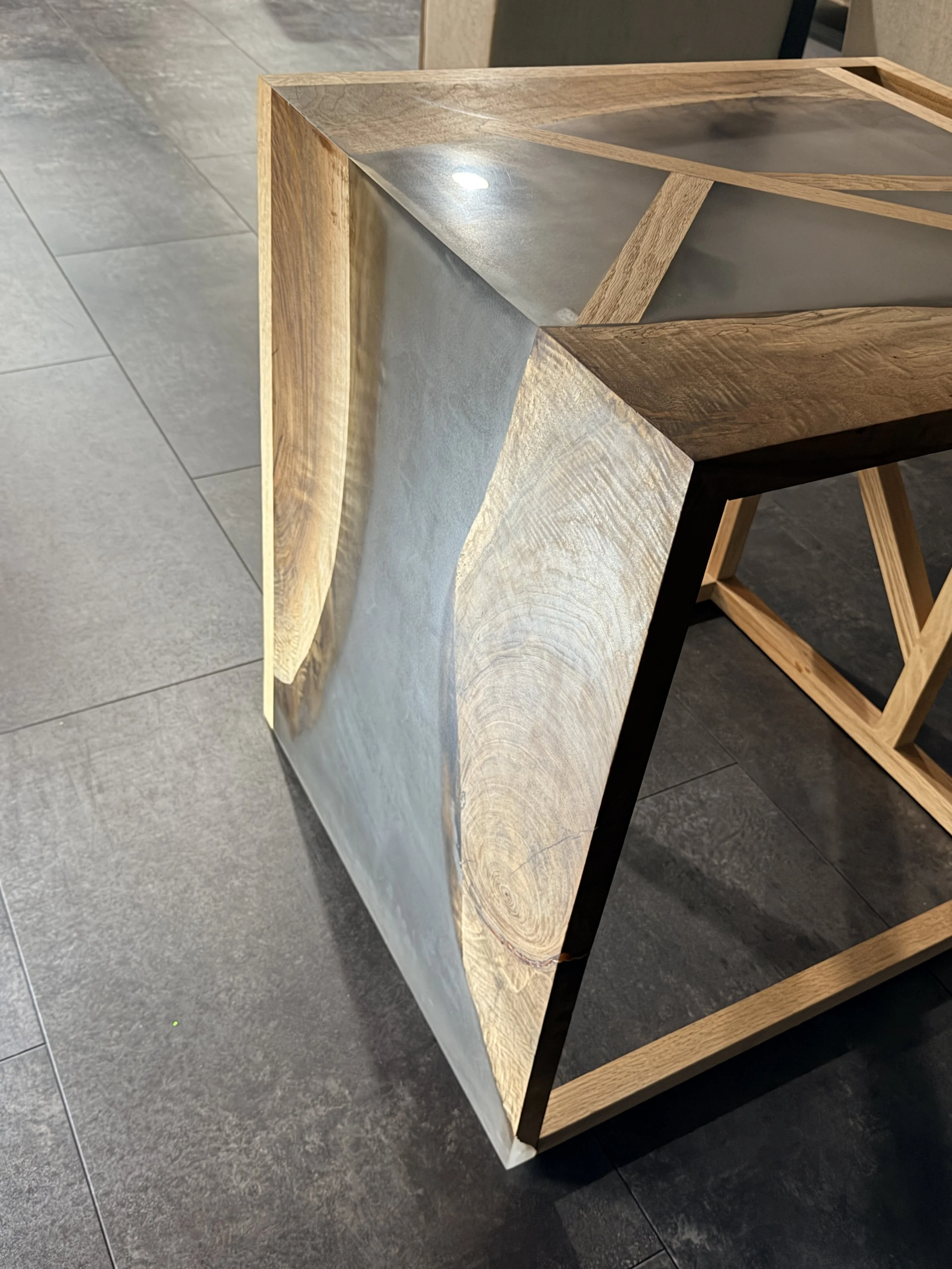 Close-up of a modern wooden and concrete side table with a geometric design, placed on a tiled floor.