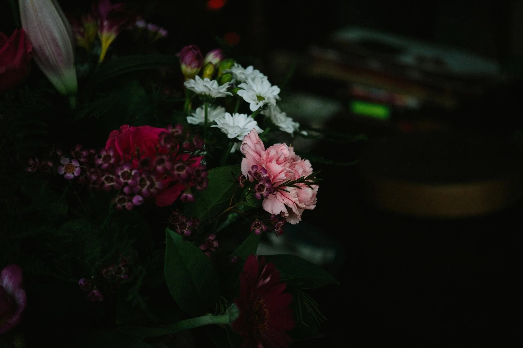 Dark image showing a bouquet of various flowers, including white, pink, and purple blooms.