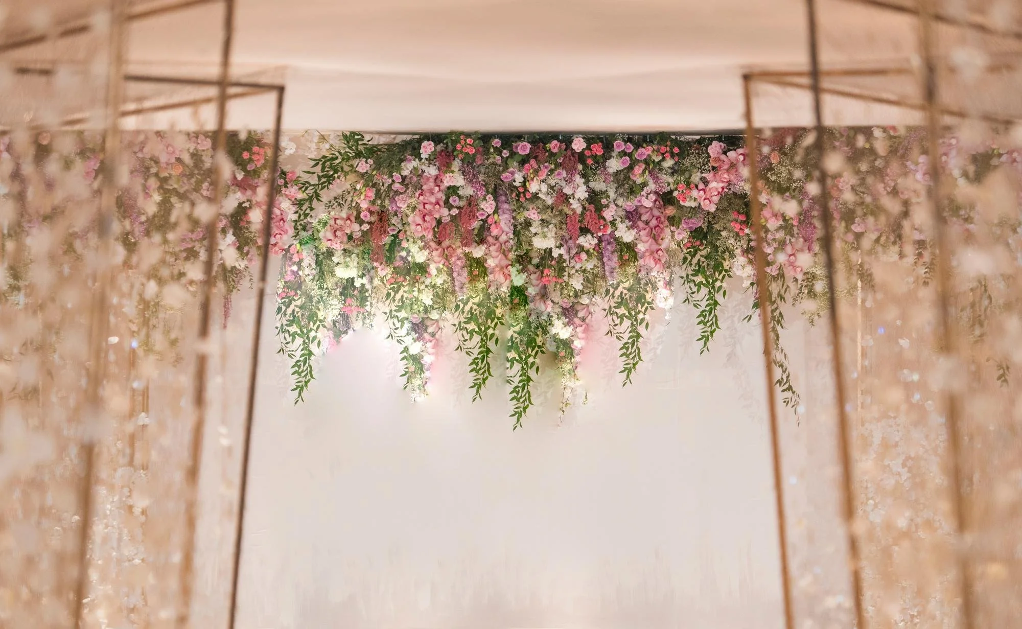 Floral arrangement of pink and purple flowers with green leaves, viewed from below through a gold wireframe structure.