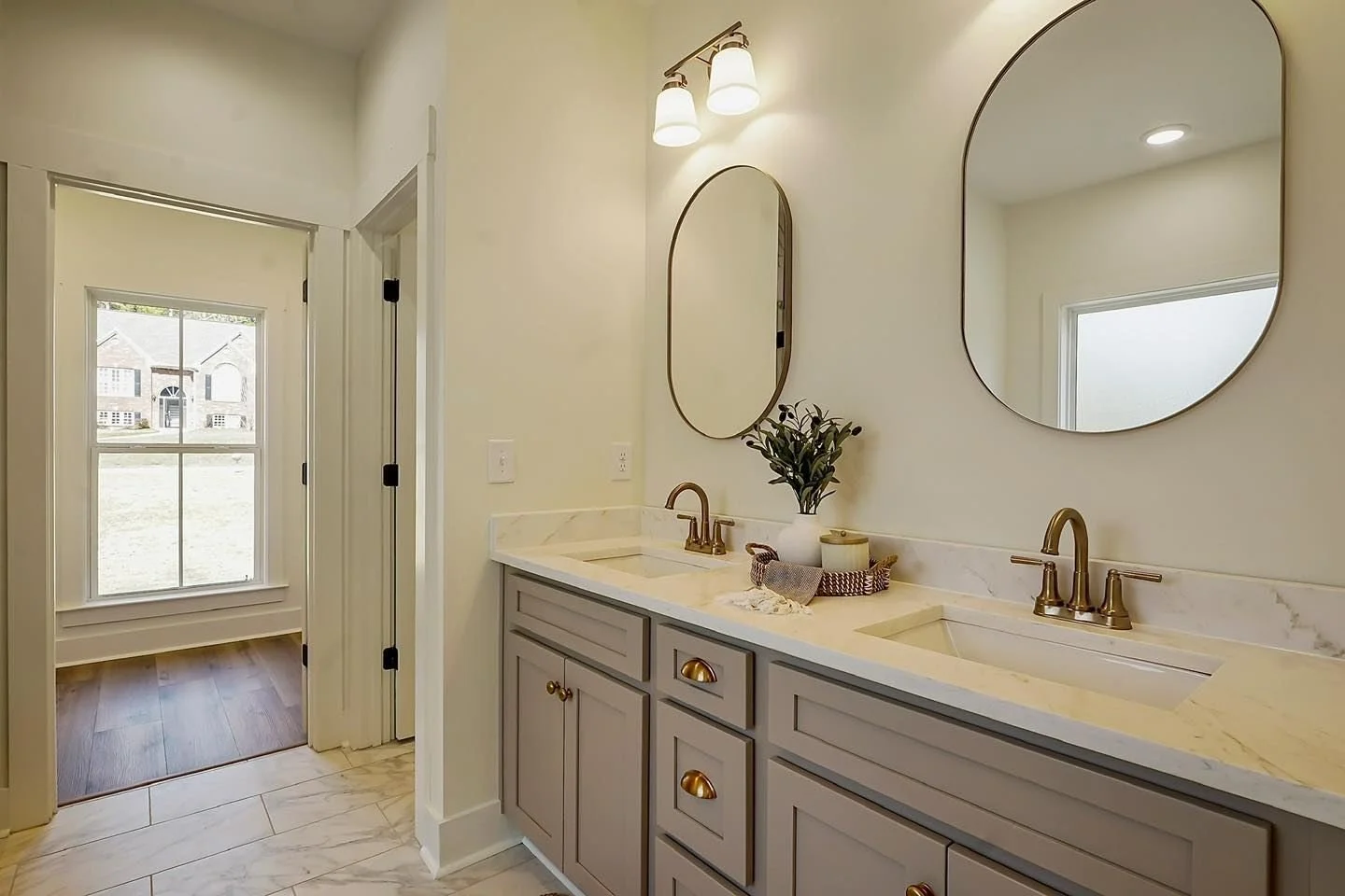 Double vanity bathroom with two oval mirrors, gold faucets, and a potted plant on the countertop. New build in birmingham alabama, build your dream house with Littleton Residential in the Greater Birmingham area