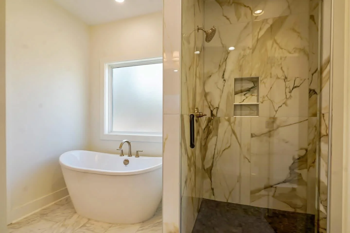 Bathroom with a freestanding bathtub next to a window and a walk-in shower with marble walls and a built-in shelf.