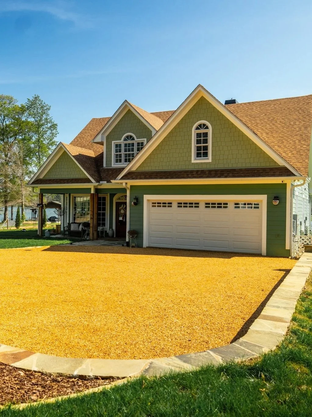 A two-story suburban house with green siding, a brown shingle roof, a attached garage, and a yellow gravel driveway. There is a walkway bordered with stone pavers leading to the house. New build in Birmingham and Shelby Alabama