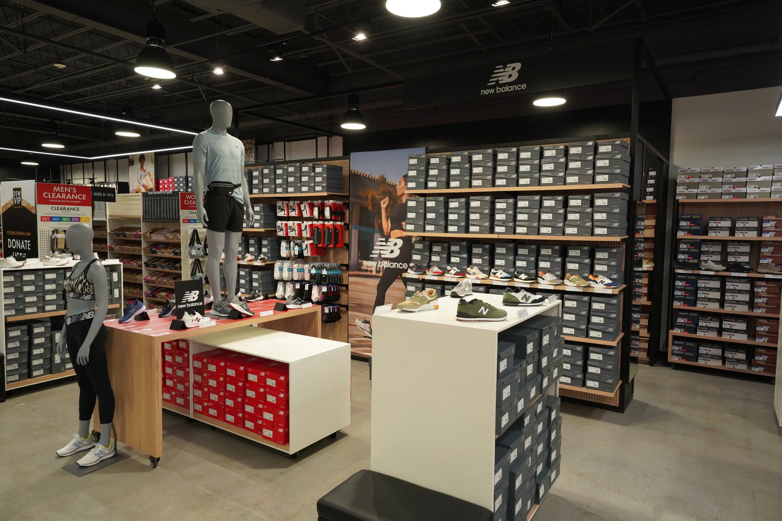 Inside a retail store displaying various athletic shoes and clothing, mannequins dressed in athletic apparel, shoe boxes stacked on shelves, a large advertising poster, and sale signs.