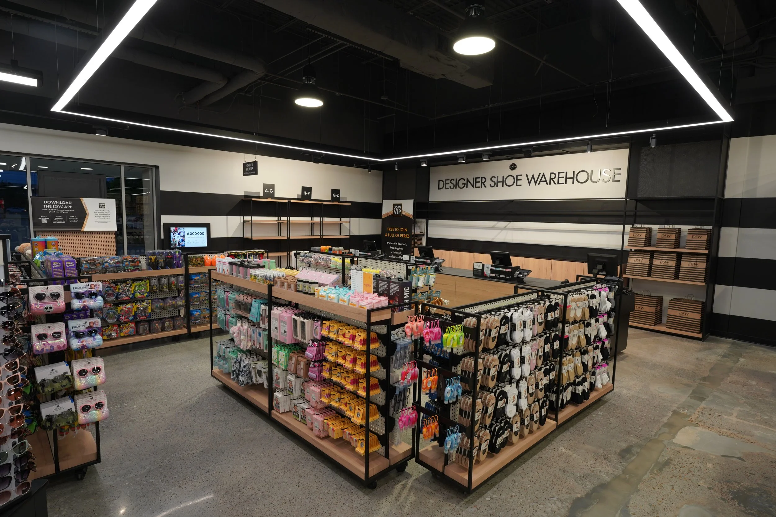 Interior of a designer shoe warehouse store with display shelves holding various colorful accessories and footwear, check-out counters at the back, and a sign reading 'DESIGNER SHOE WAREHOUSE' on the wall.
