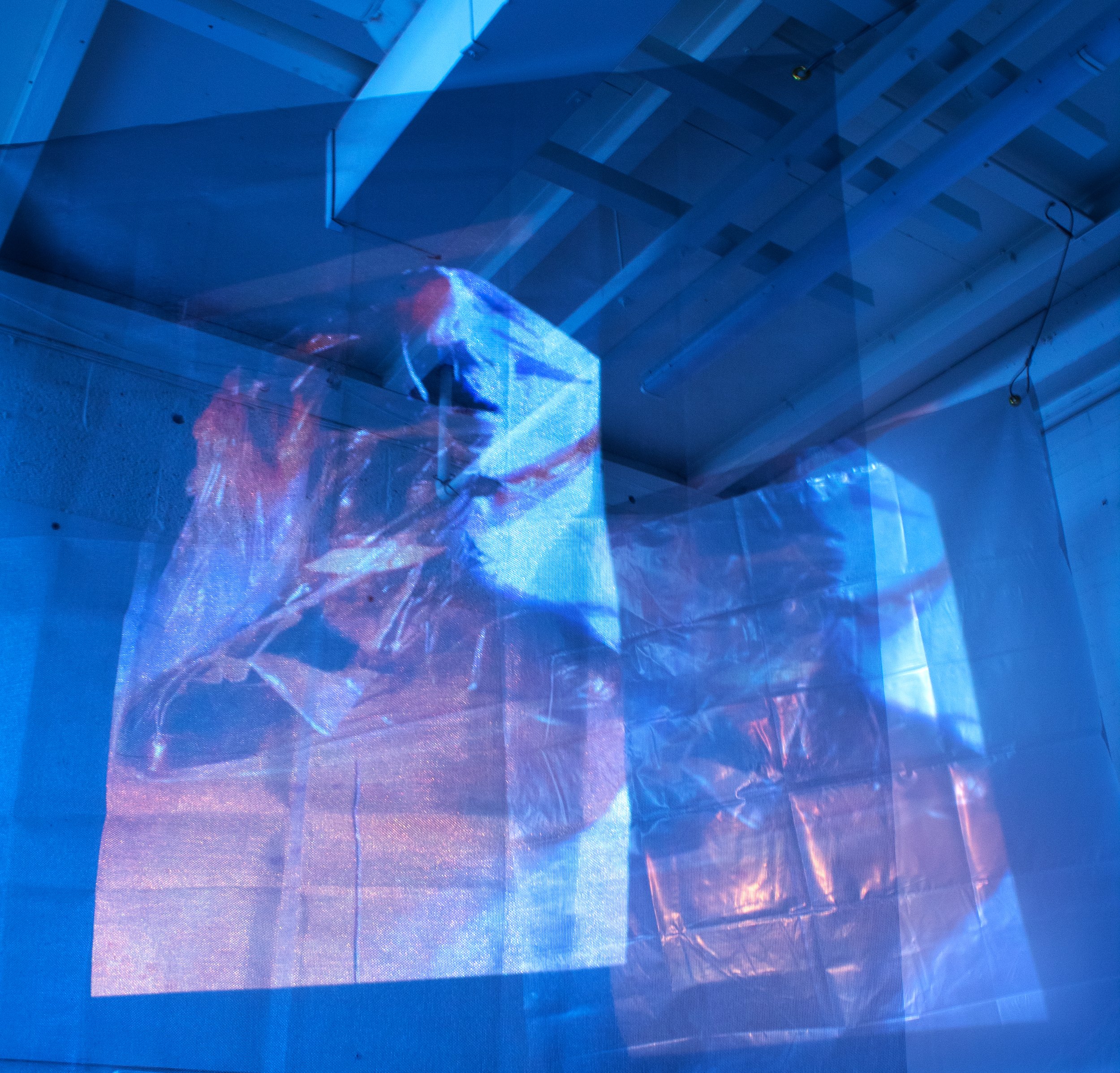 Abstract digital art installation with blue and red hues, featuring projected images on crinkled translucent material in a modern, industrial space.