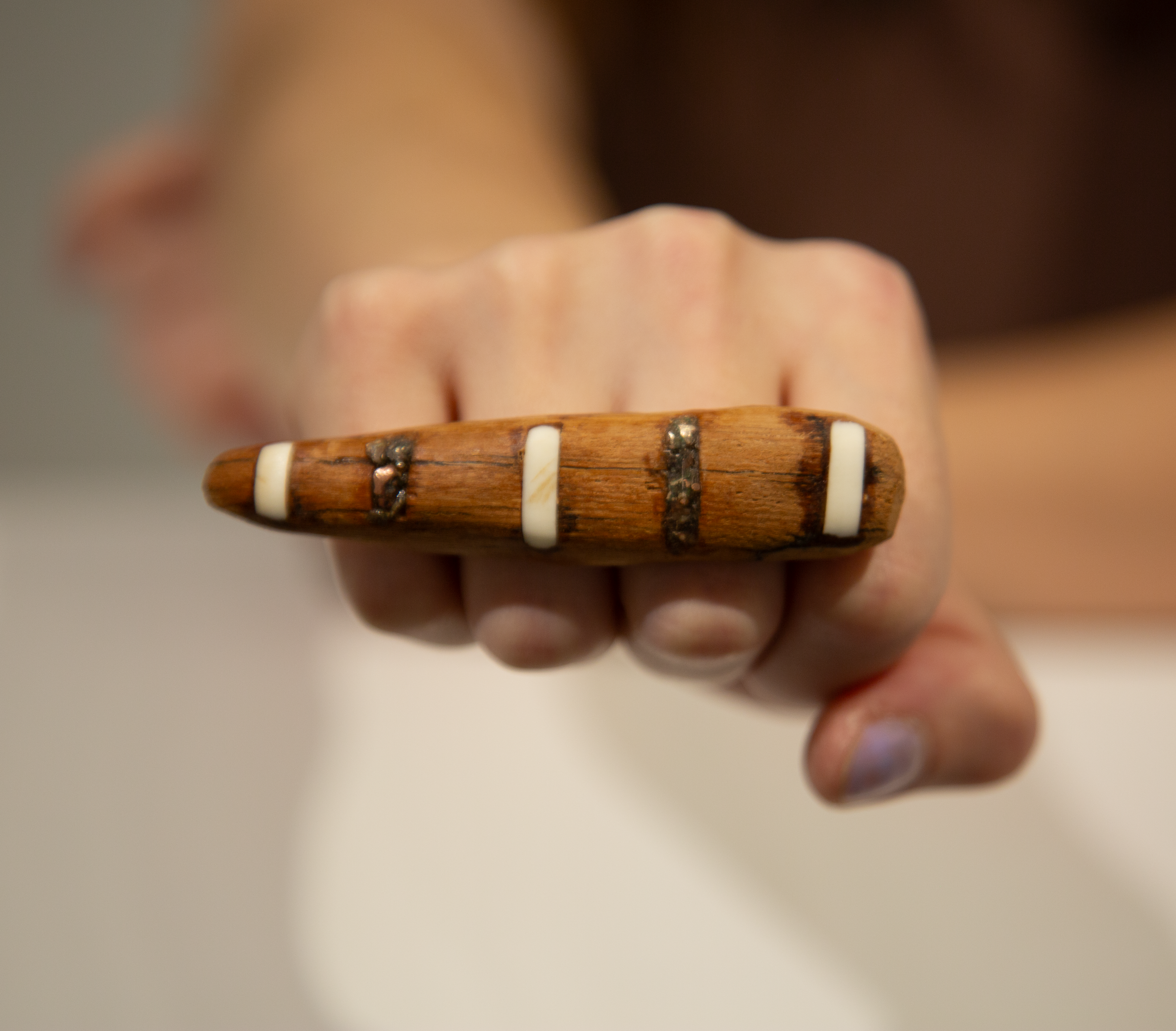 Close-up of a person's hand holding a wooden ring with white and dark brown beads, with blurred background and face partially visible in profile.