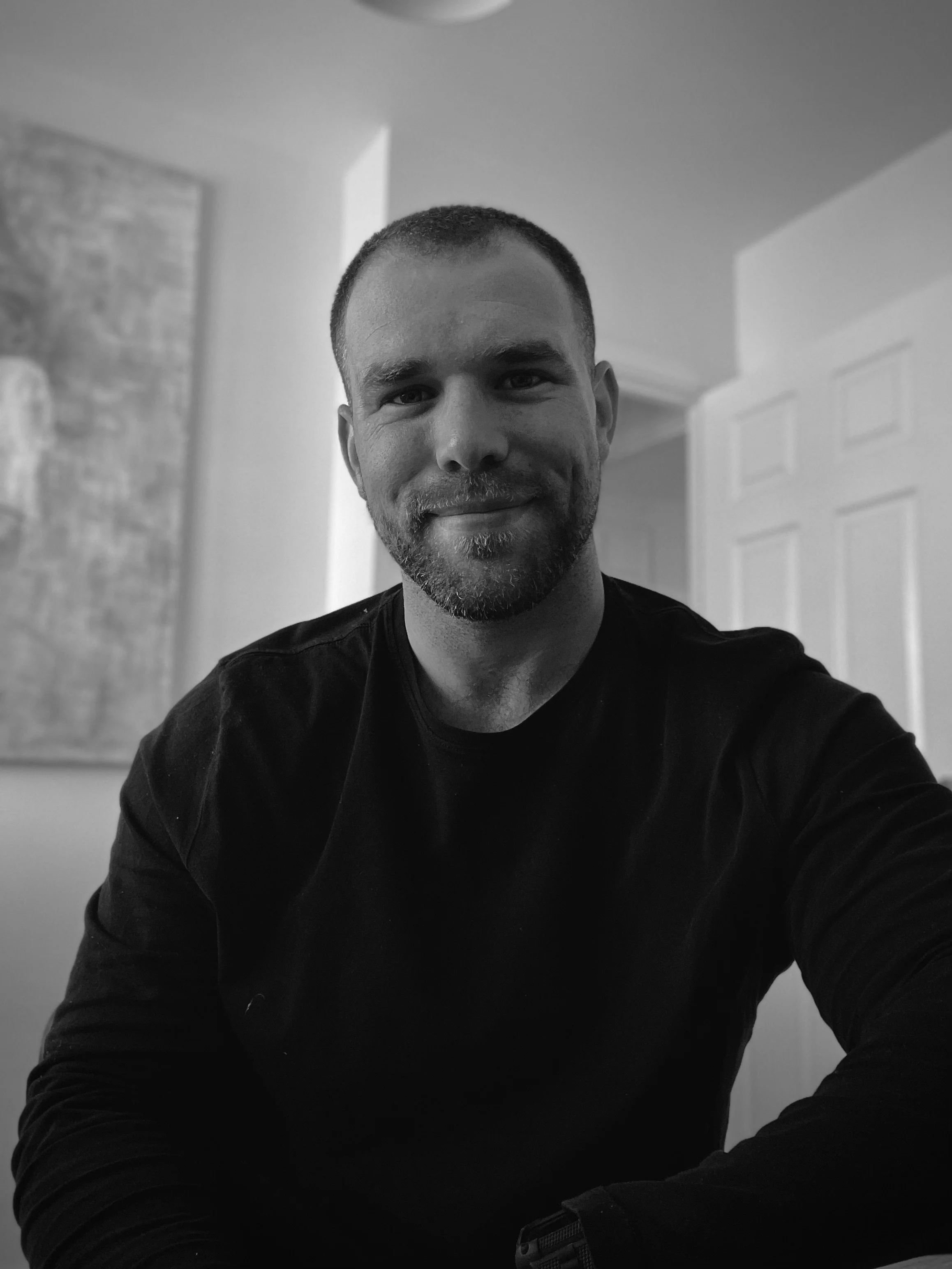 Black and white portrait of a man smiling, wearing a dark shirt, indoors.