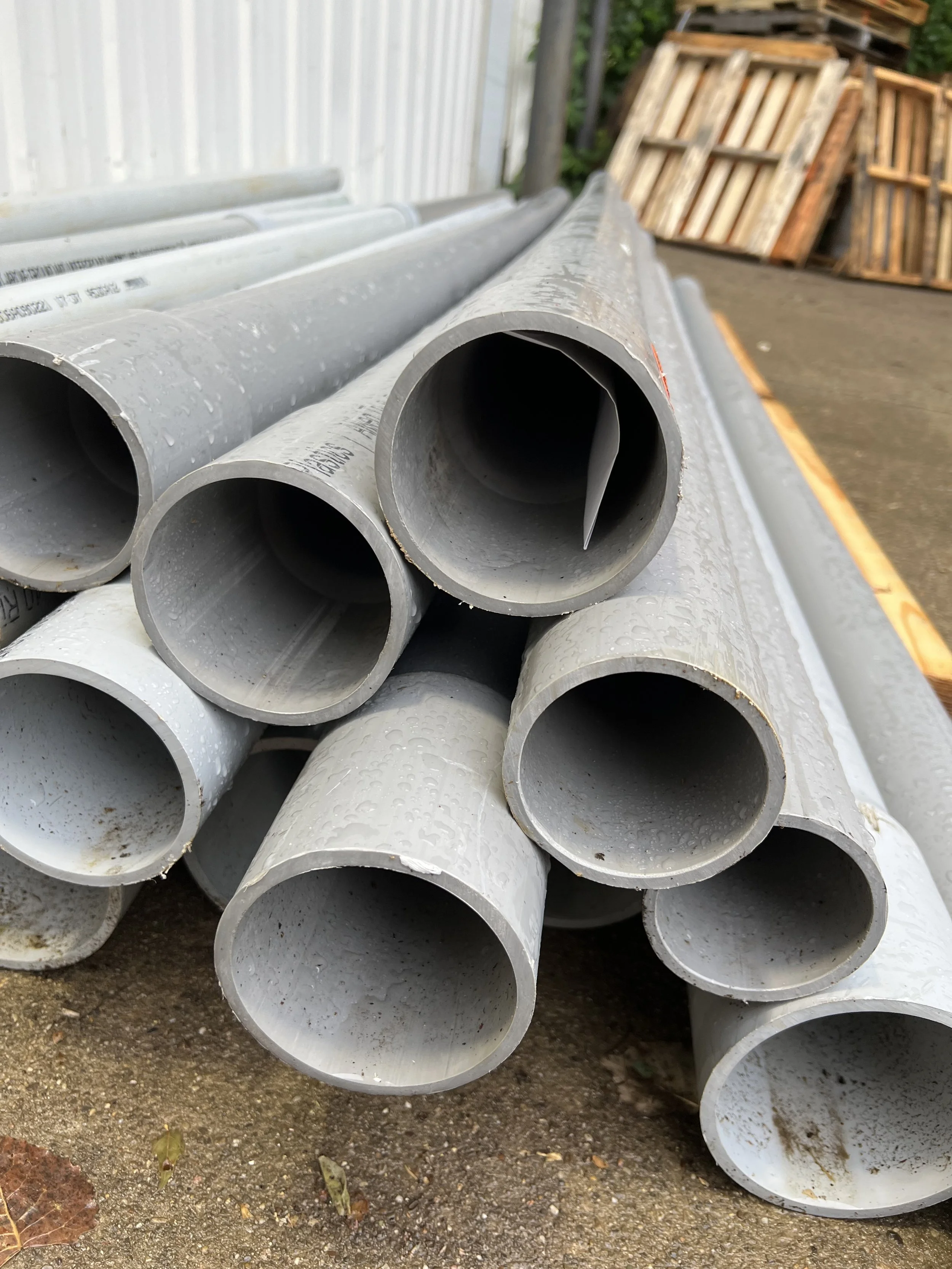 PVC pipes stacked outdoors on concrete ground near a wall.