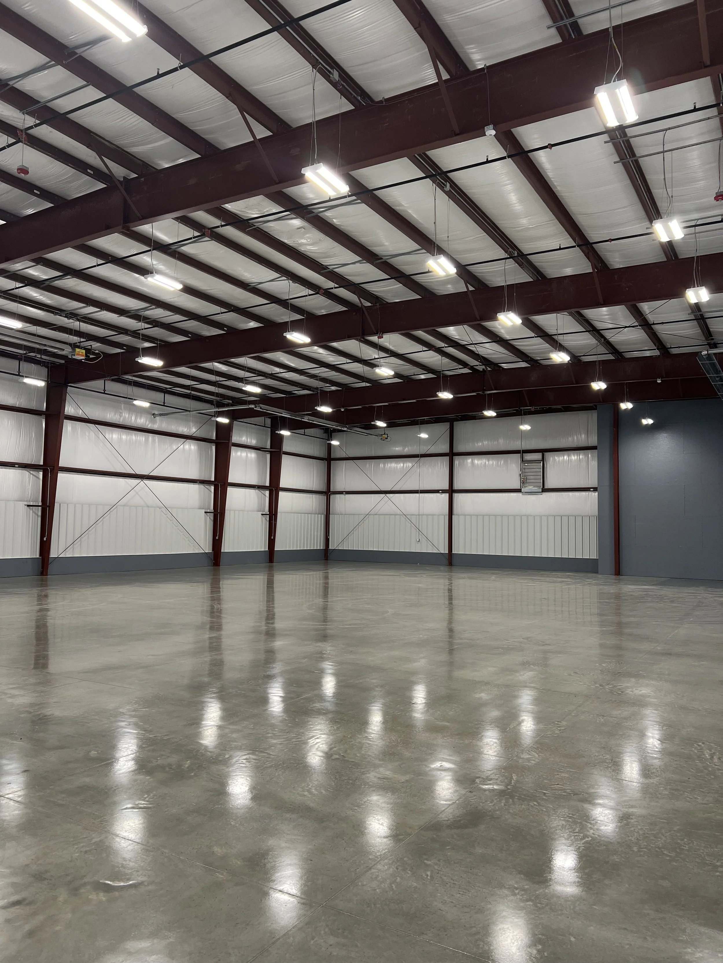 Empty warehouse interior with concrete floor, metal beams, and overhead lighting