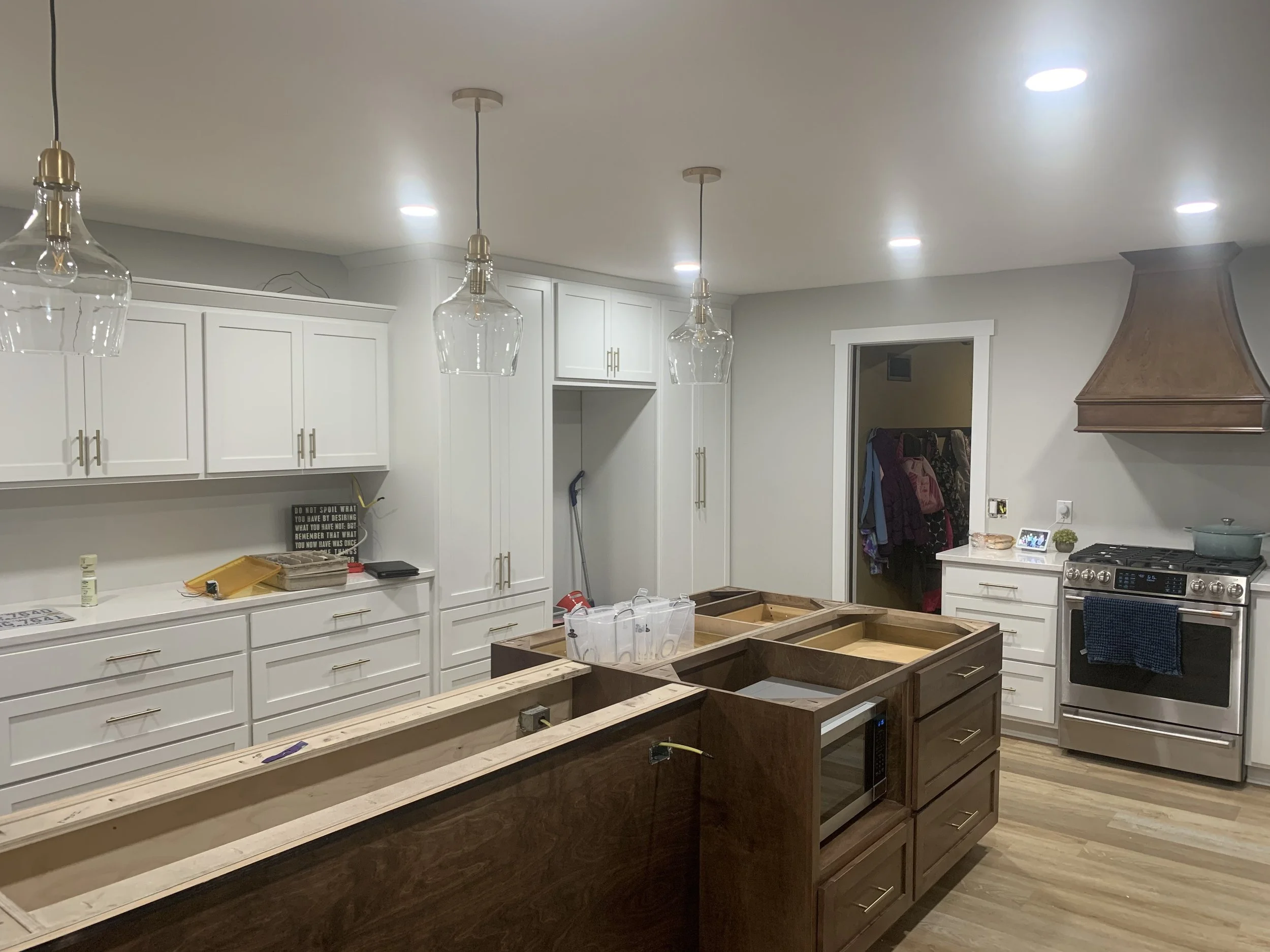 Modern kitchen under renovation with white cabinets, wooden kitchen island, glass pendant lights, and stainless steel appliances.