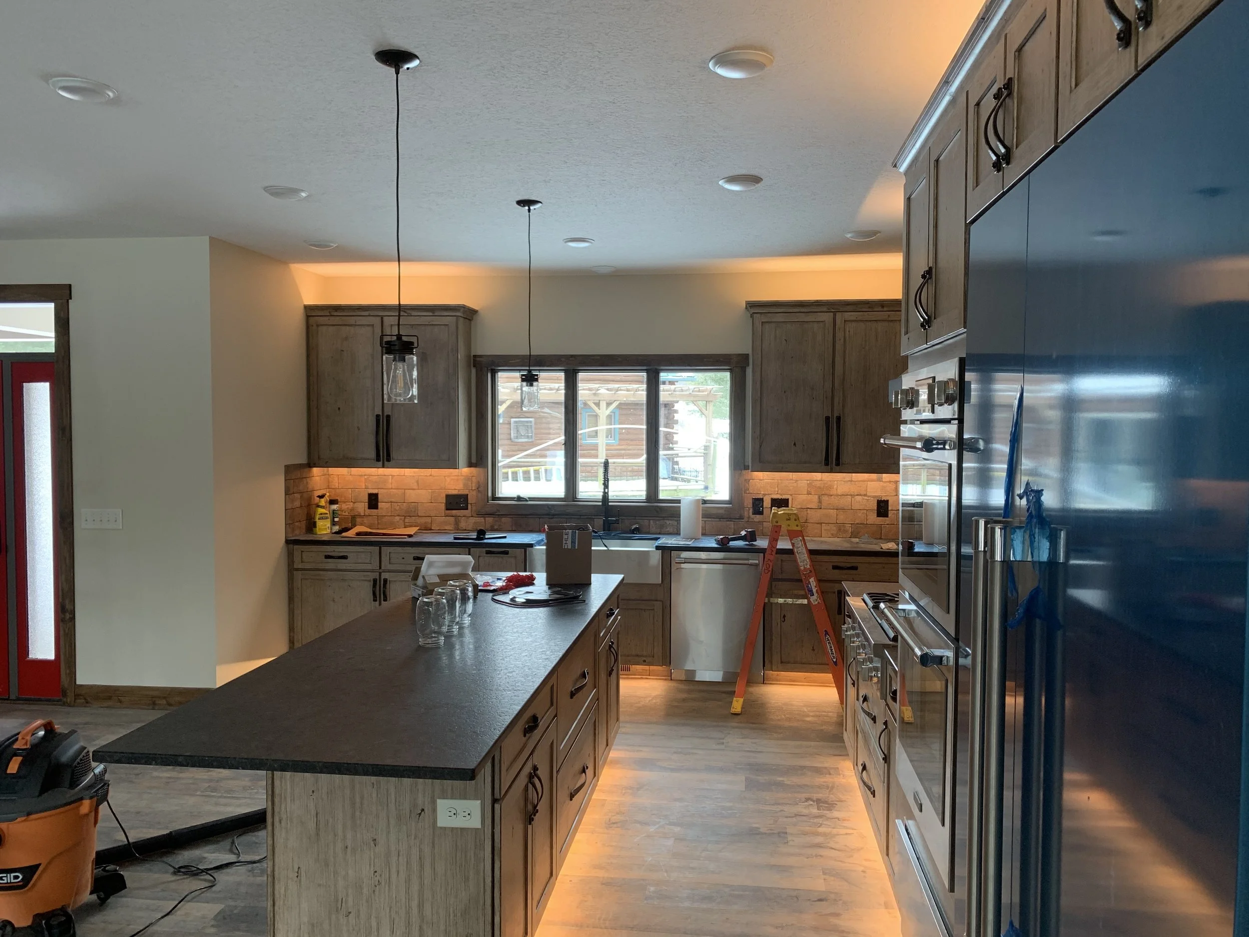Modern kitchen with wood cabinetry, island, pendant lights, and stainless steel appliances, under construction.