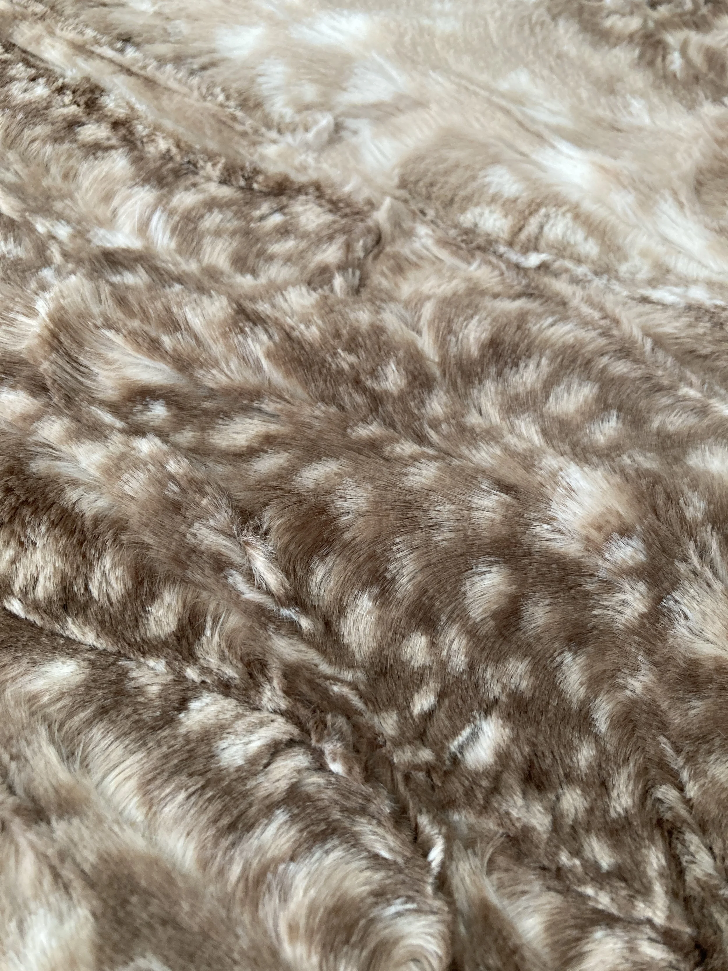 A folded baby blanket resting on a light wood surface. The top fold displays a whimsical woodland animal pattern with foxes, deer, and squirrels on a soft, pale blue background.