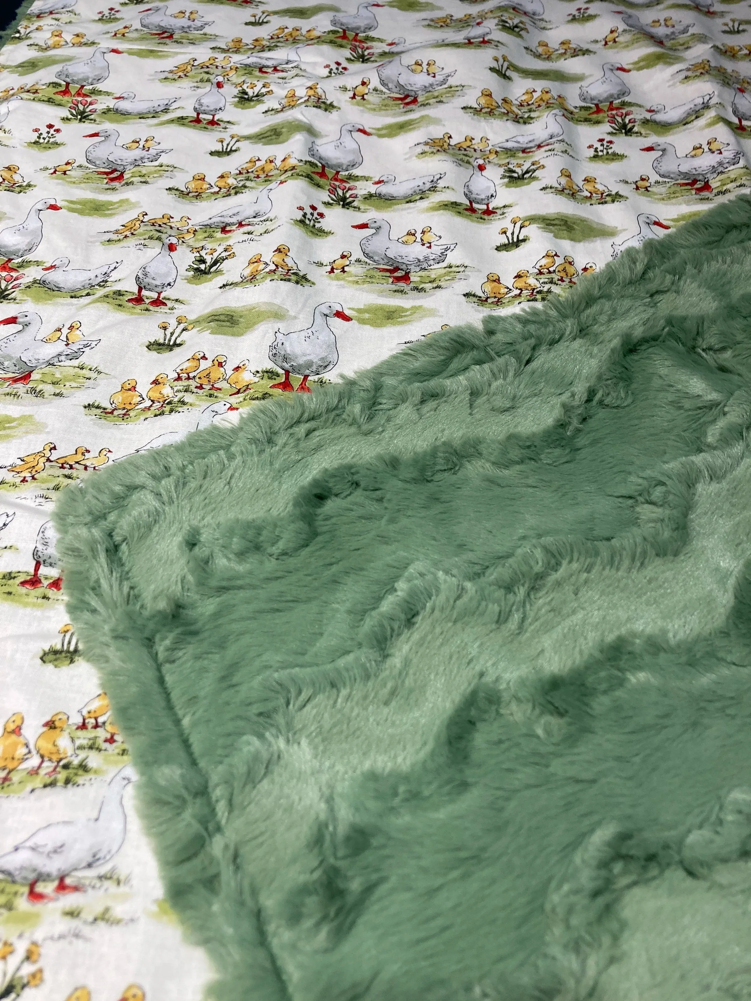 Softly folded handmade baby blanket showing the contrast between the white Mother Goose cotton print and the textured sage green Shannon Fabrics minky reverse