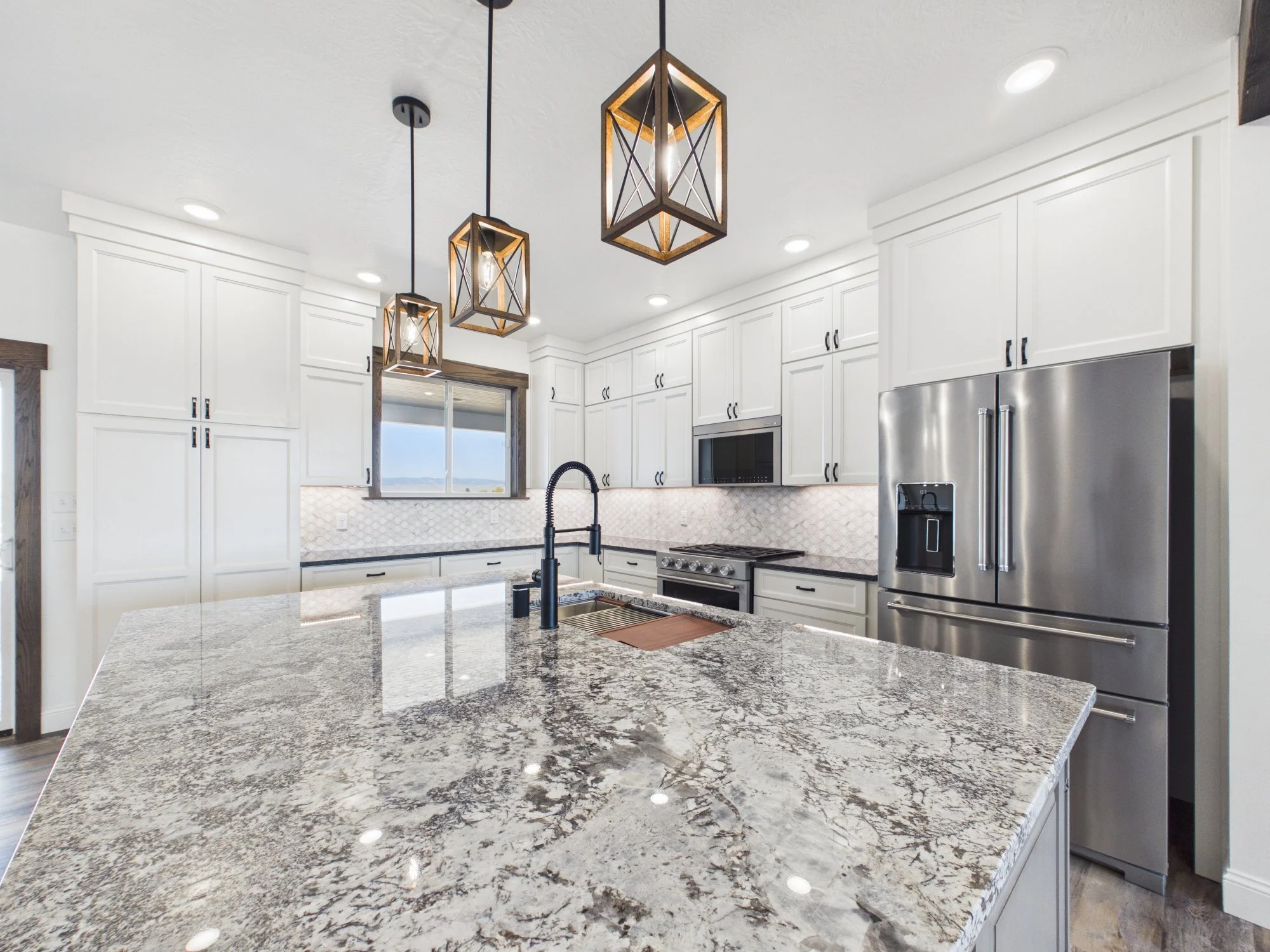 Modern kitchen with white cabinets, granite countertops, stainless steel appliances, and pendant lights.