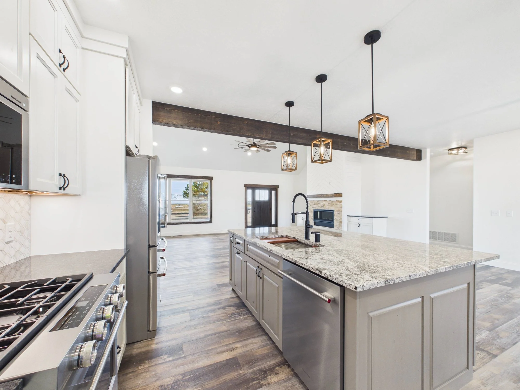 Modern kitchen with white cabinets, a marble countertop island, pendant lights, stainless steel appliances, wood flooring, and a ceiling fan.