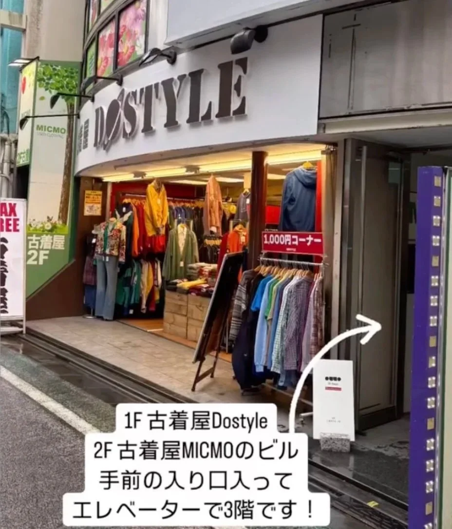 Storefront of a clothing shop named Dostyle, with clothing racks outside and a vending machine to the right, adjacent to an elevator entrance.