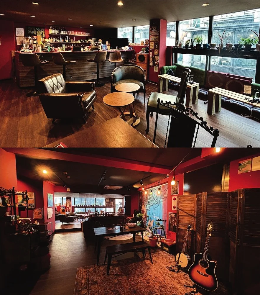 A cozy coffee shop or lounge with a bar, seating area with armchairs and small tables, large windows, and musical instruments, including guitars, in a vibrant, artsy atmosphere.