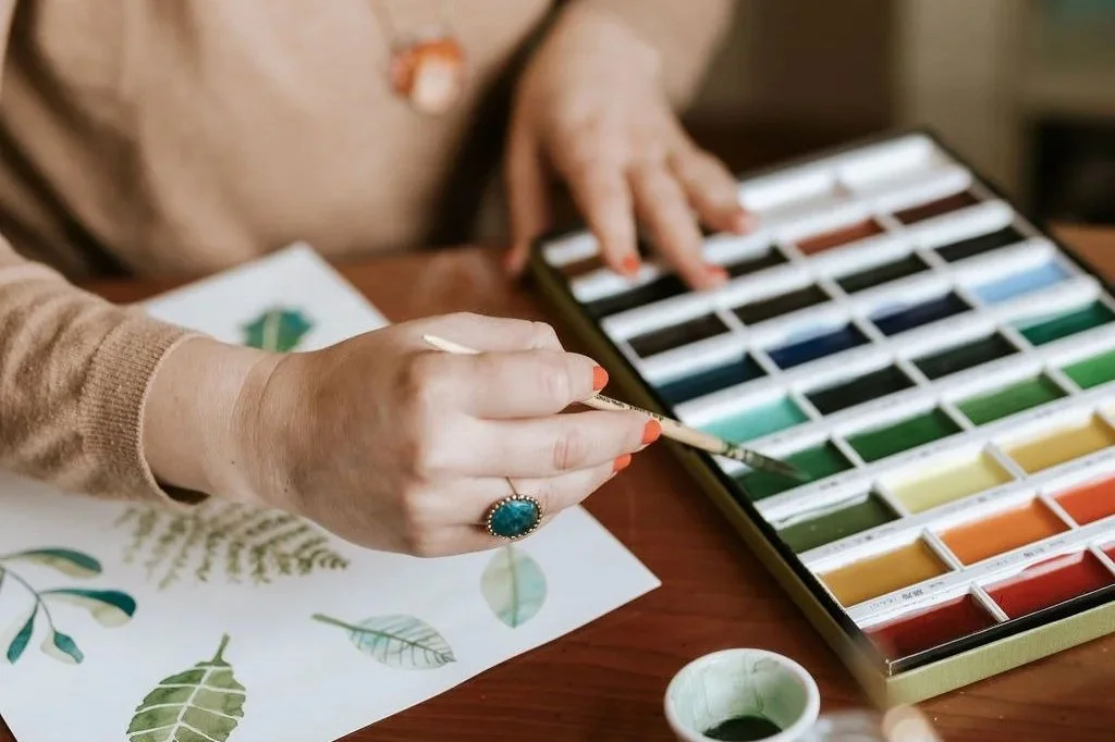Persona che dipinge con acquerelli su carta con foglie e fiori.