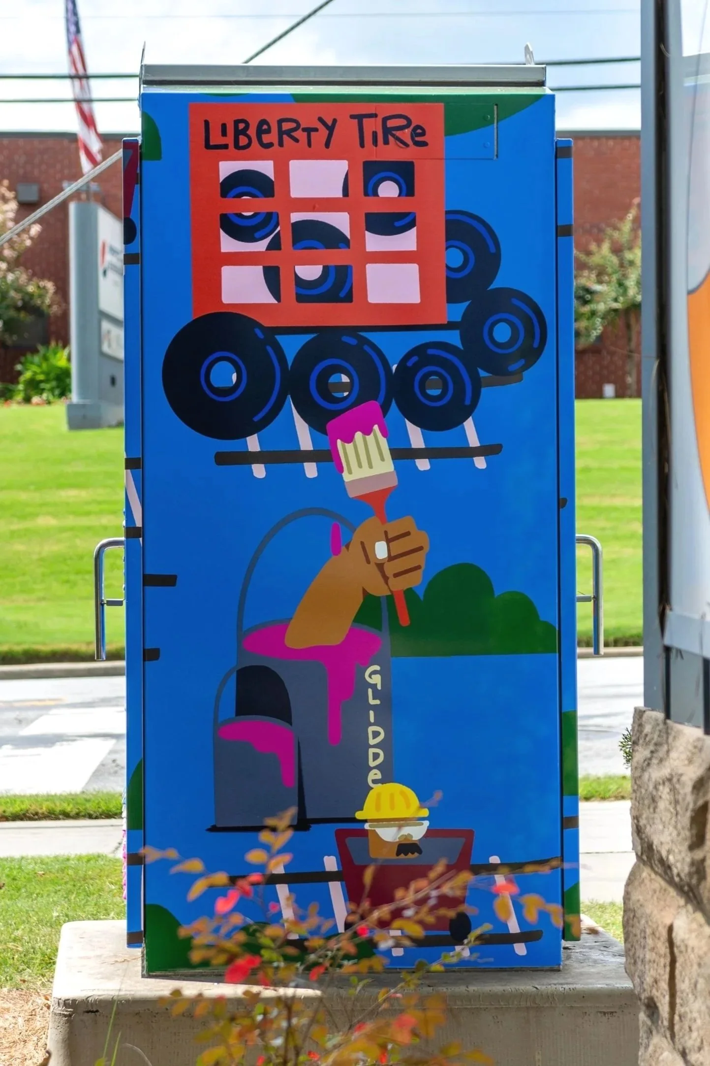 Colorful advertising poster for Liberty Tire featuring a cartoon hand holding a paintbrush, a mailbox with dripping pink paint, and black tires on a blue background.