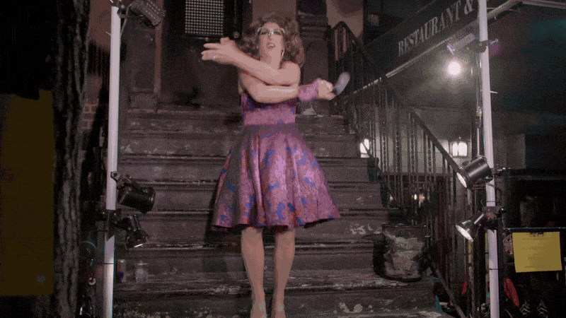 Woman in a purple patterned dress dancing on a staircase, with stage lights on either side.