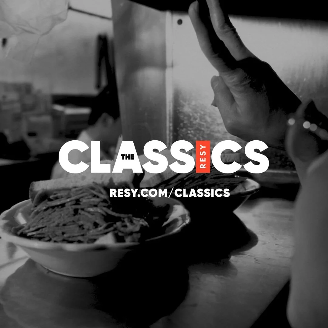 Black and white photo of a bowl of noodles and a person's hand reaching for the bowl, with some text overlay promoting Classic recipes at resy.com/classics.