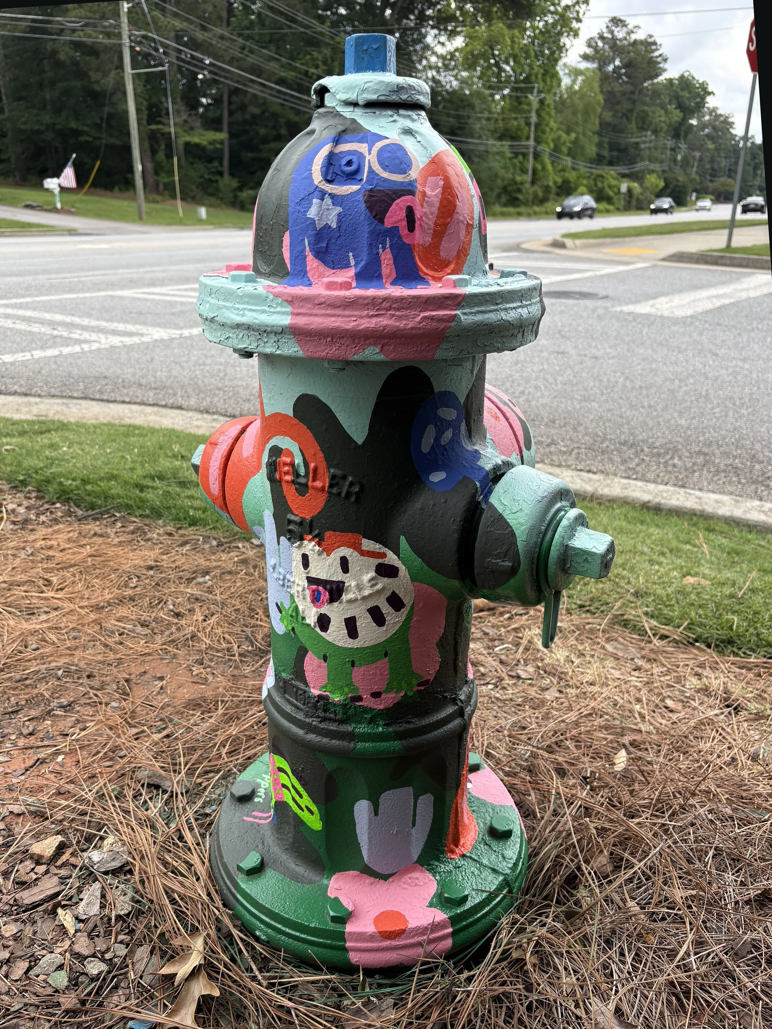 Decoratively painted fire hydrant with colorful cartoon-style characters and designs, including a blue creature with glasses, a clock, and a smiling figure.