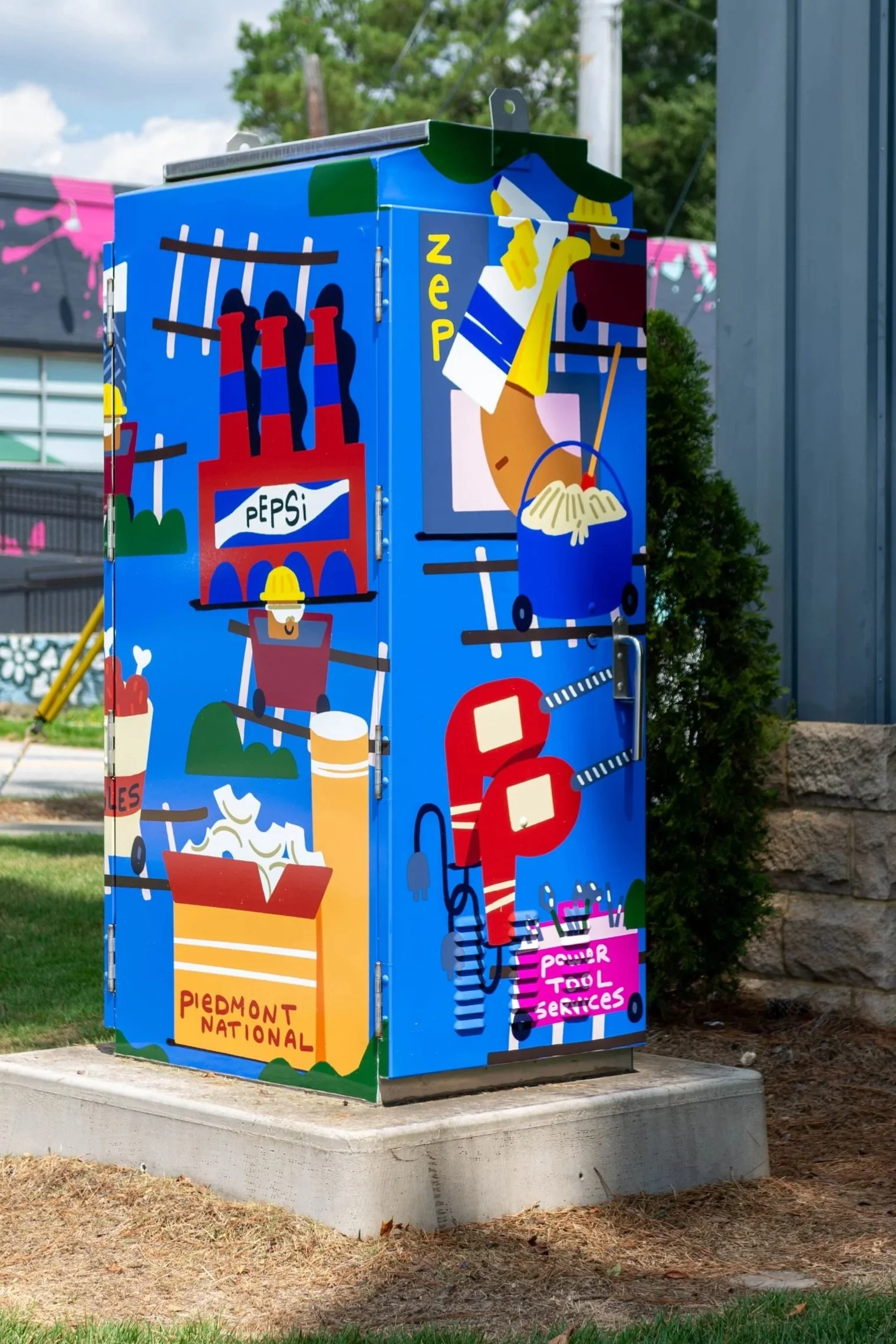 Colorful outdoor utility box decorated with illustrations of construction tools, a food container, a soda bottle, and the words 'Piedmont National', 'Power Tool Services', and 'PEPSI' on it.