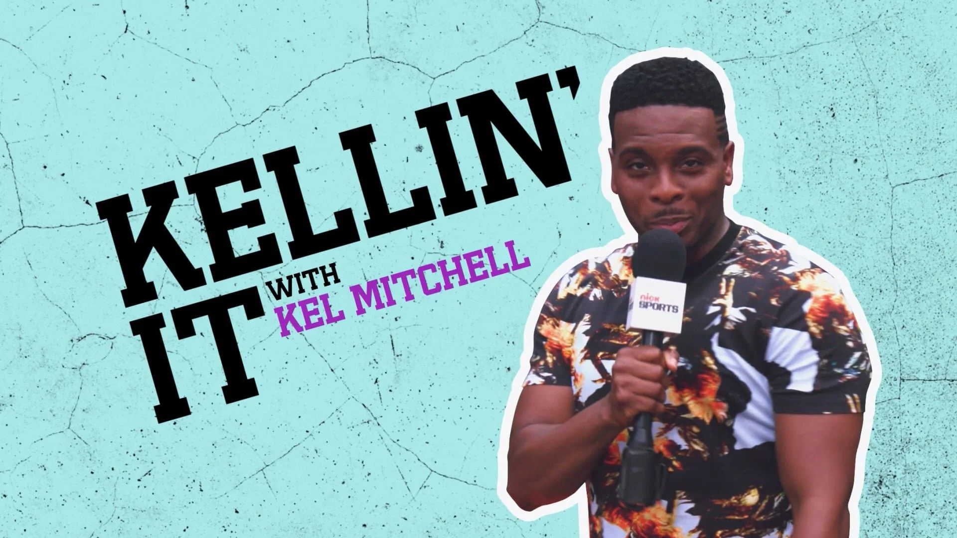 A man holding a microphone with a clip that says 'FOX SPORTS'. He is wearing a colorful floral shirt and looking at the camera. Behind him is a teal, cracked wall with text that says 'KELLIN IT' in large black letters and 'with KEL MITCHELL' in smaller purple letters.