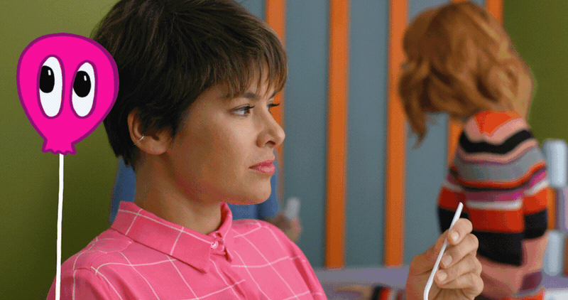 A woman in a pink shirt holding a white straw with a colorful background and a girl with red hair in a striped sweater in the background.