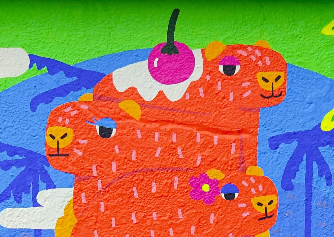 Colorful cartoon illustration of three orange tigers with different facial expressions, surrounded by blue and green foliage, with a cherry on top of one tiger.