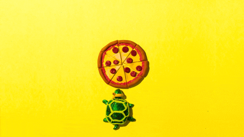 A small turtle figurine is looking up at a pizza slice on a core, placed on a bright yellow background.