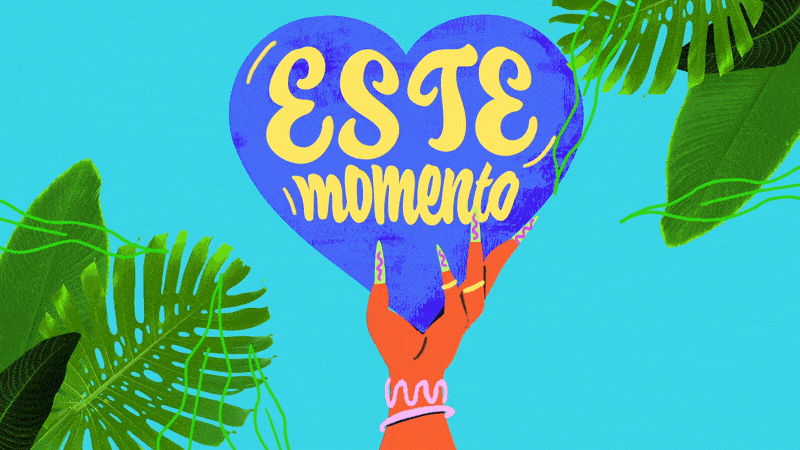 A hand holding a blue heart-shaped sign with yellow text that reads 'Este momento,' surrounded by green tropical leaves on a light blue background.