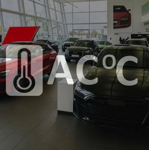 Several luxury cars displayed inside a spacious car dealership with large glass windows and promotional posters on the wall.