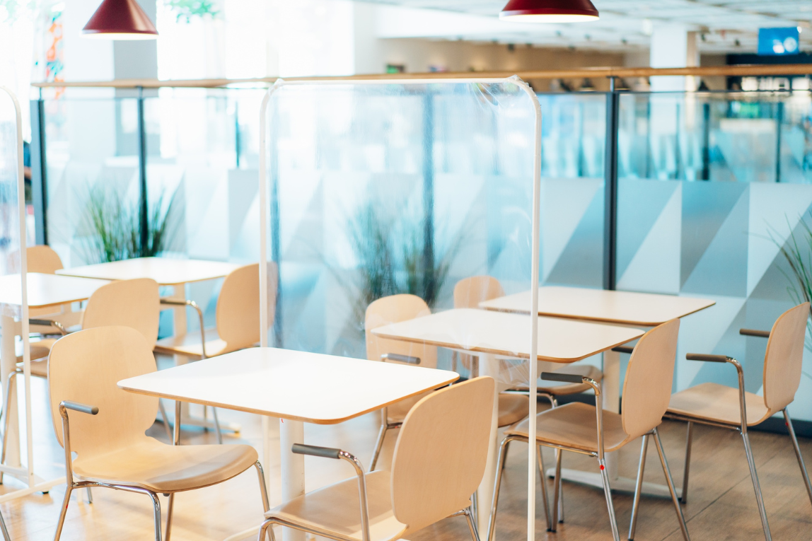 Un espace de restauration moderne avec des tables et des chaises en bois clair, séparées par des écrans en plexiglas.