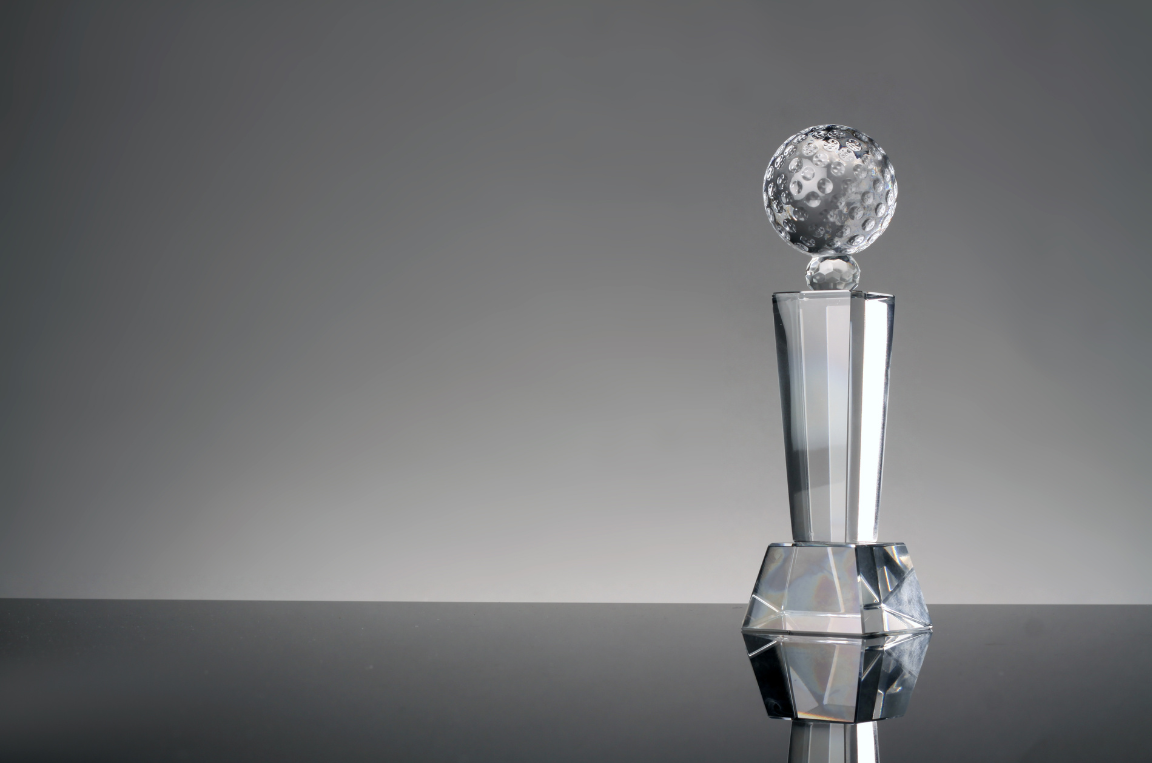 Trophée en cristal avec une boule texturée en haut, posé sur une surface réfléchissante, fond gris.