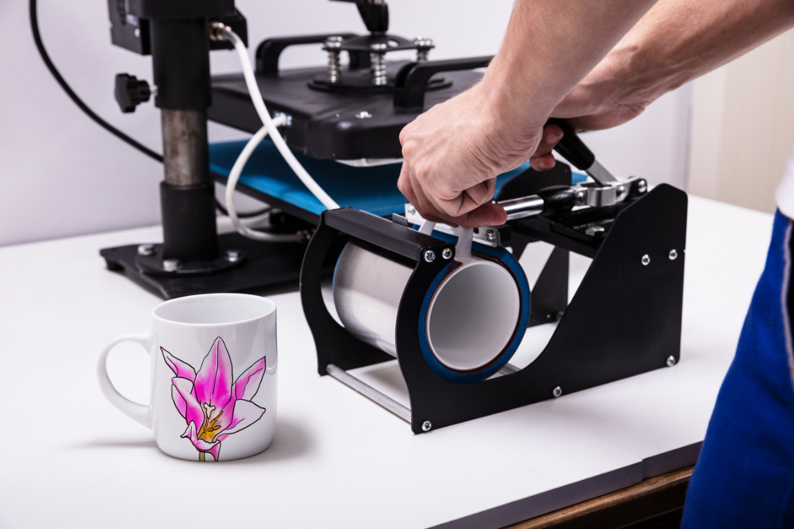 Machine de sublimation de tasse, main tenant une tasse blanche avec une fleur rose, sur une table blanche
