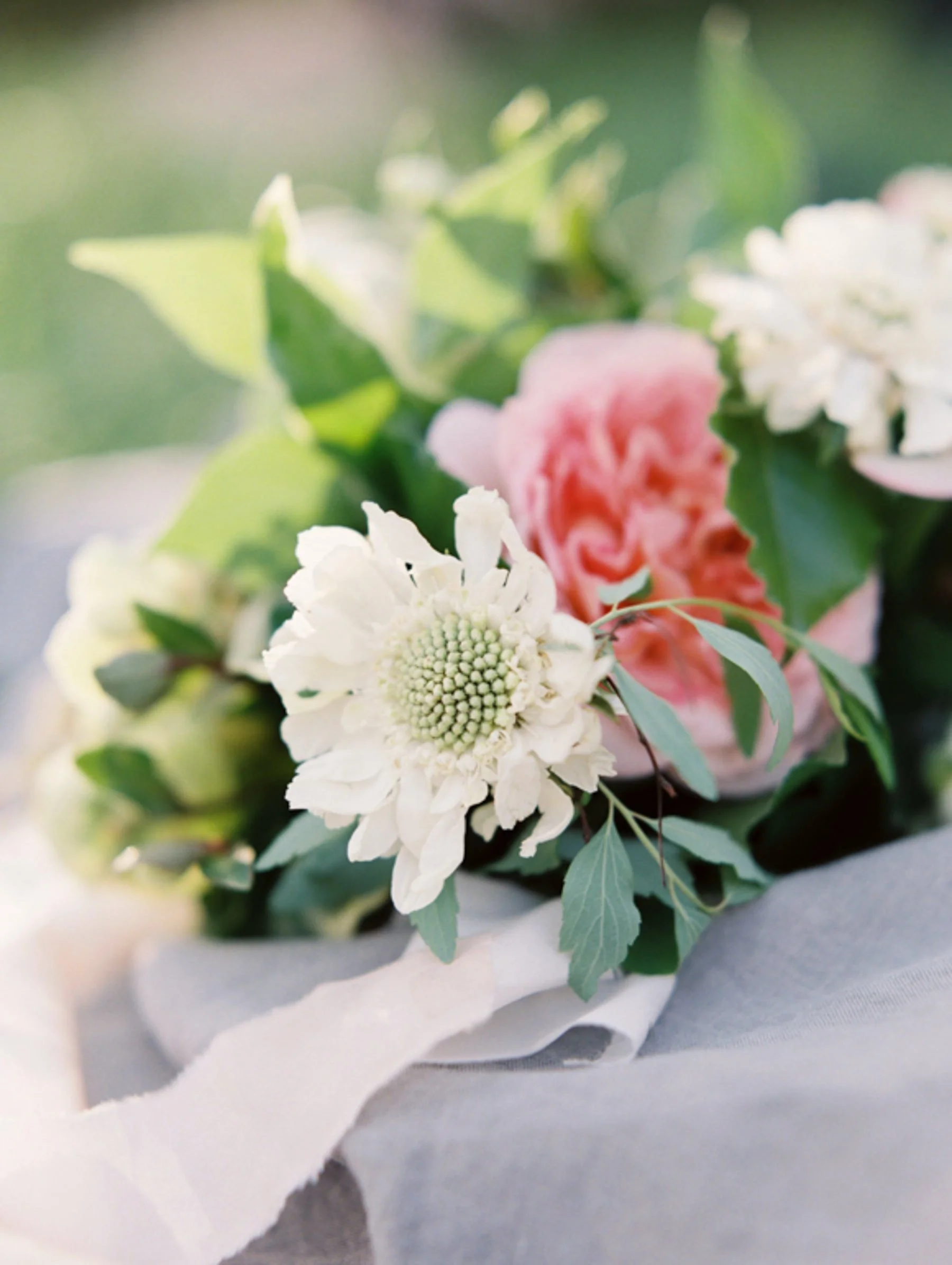Close-up of a bouquet of white and pink flowers with green leaves on gray fabric.