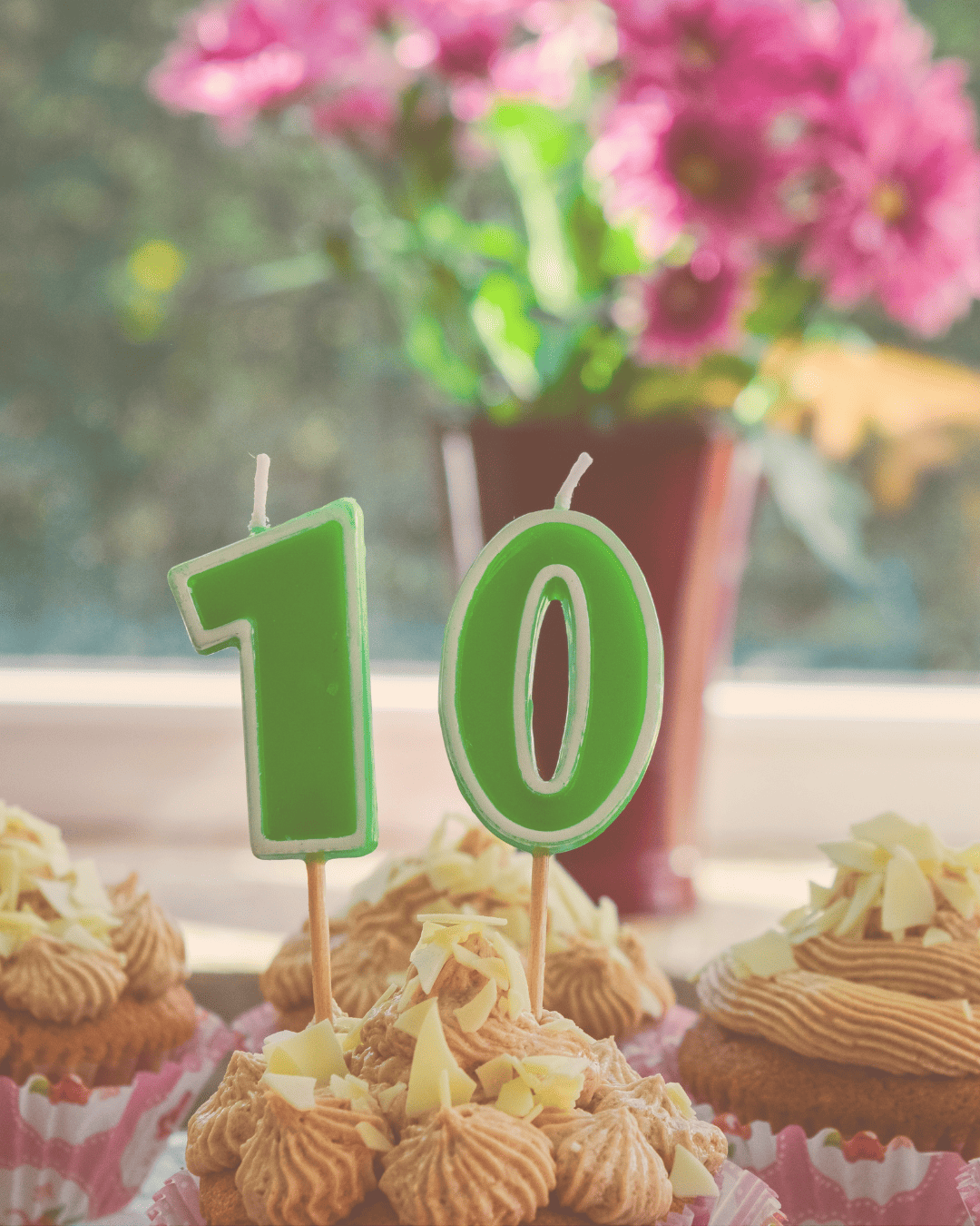 A celebratory graphic featuring green number 10 birthday candles in front of a vase of pink flowers and pastries.