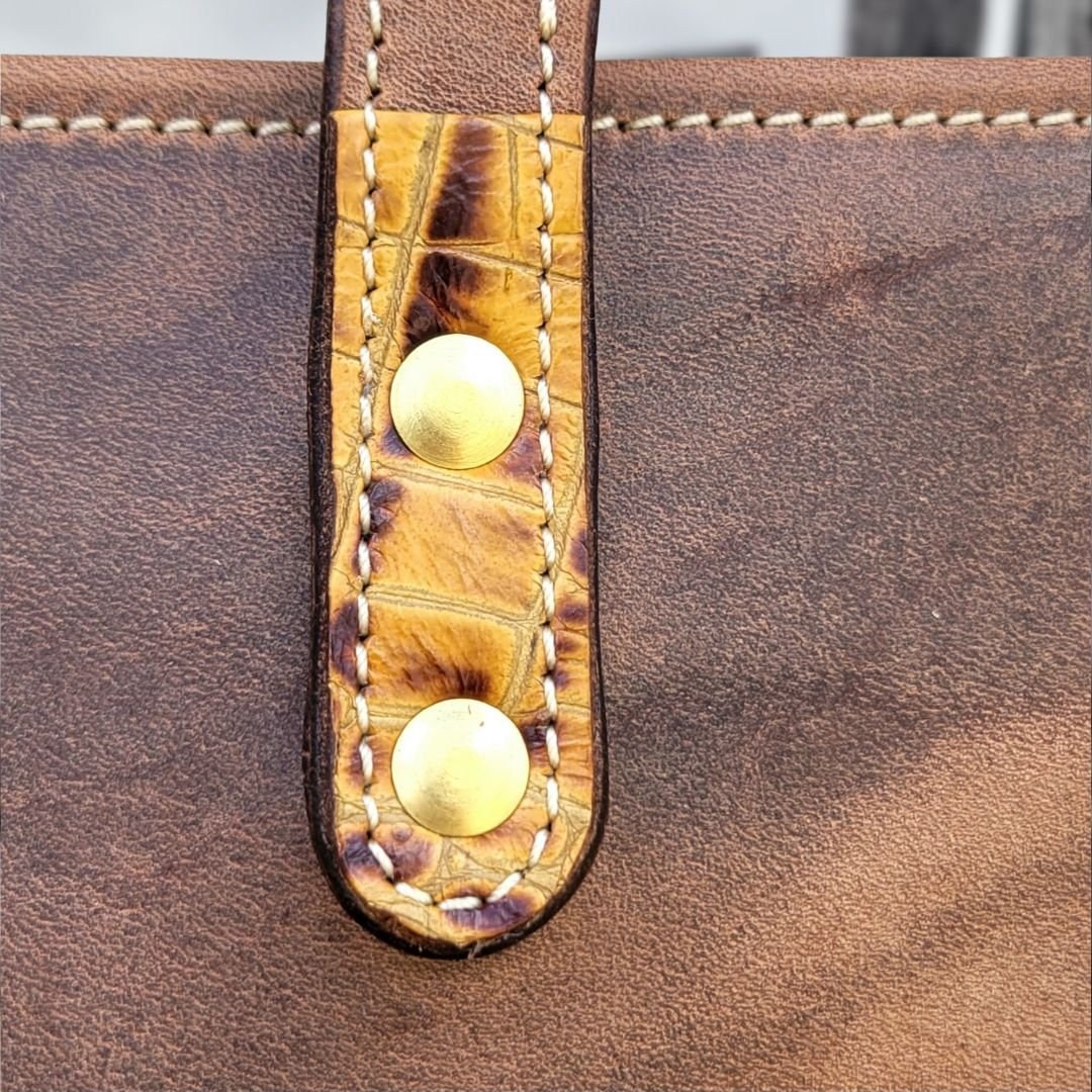 Strap detail and solid brass rivets on a leather tote bag