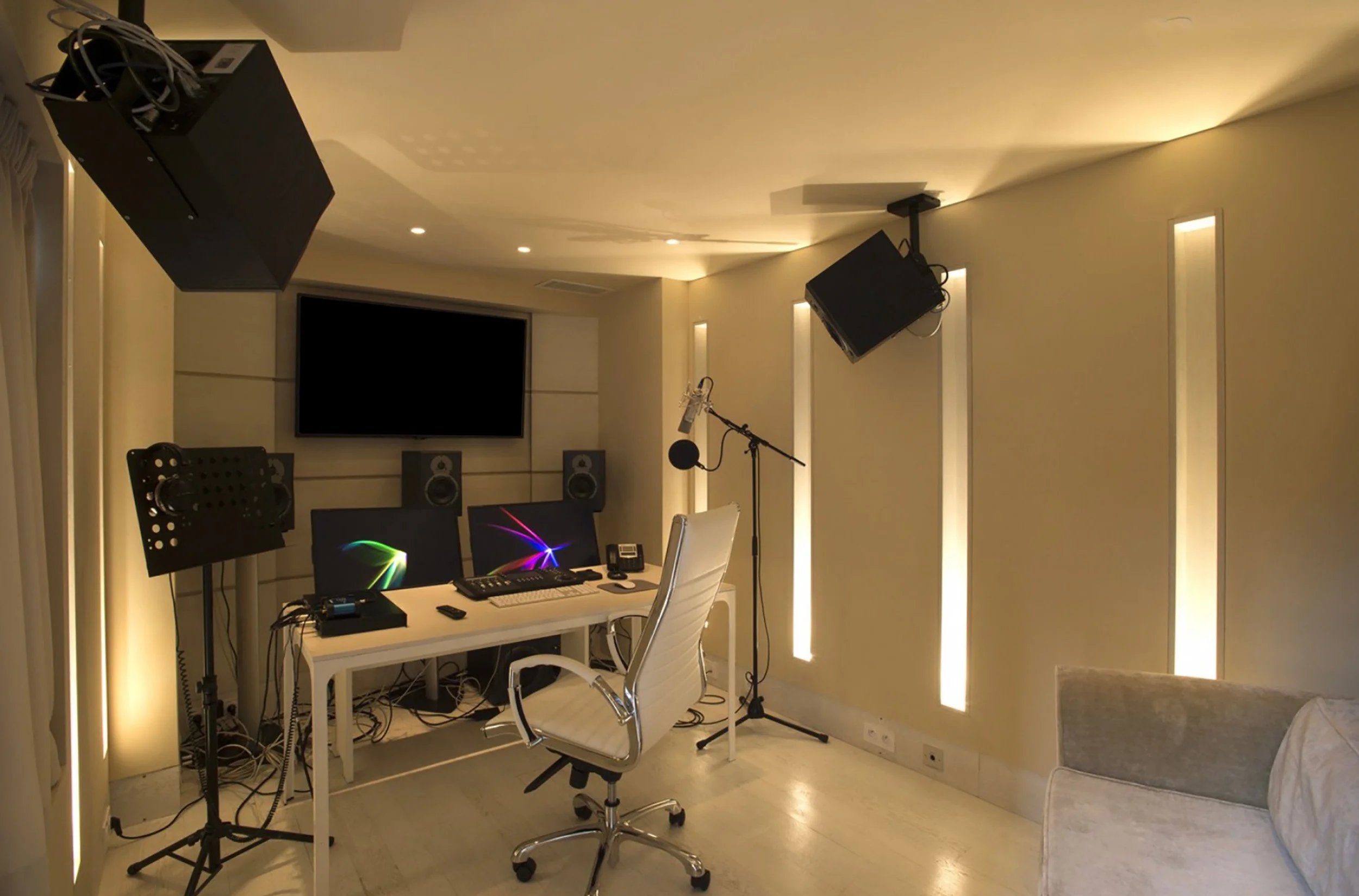 Studio d'enregistrement avec microphones, écrans, et équipement audio, mobilier blanc et éclairage tamisé.