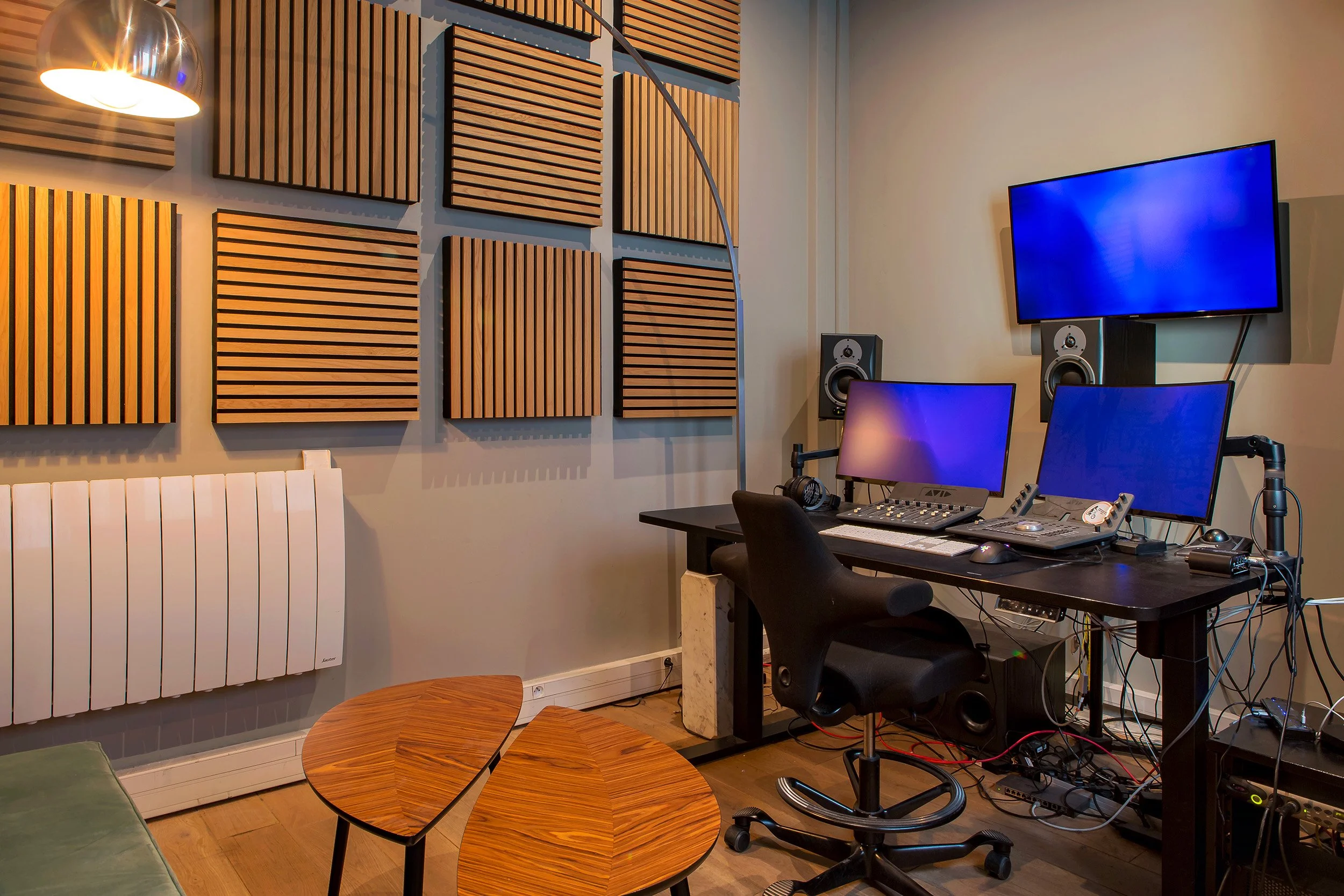 Studio d'enregistrement avec murs en bois, deux moniteurs, un clavier, une console de mixage, un fauteuil et des haut-parleurs.