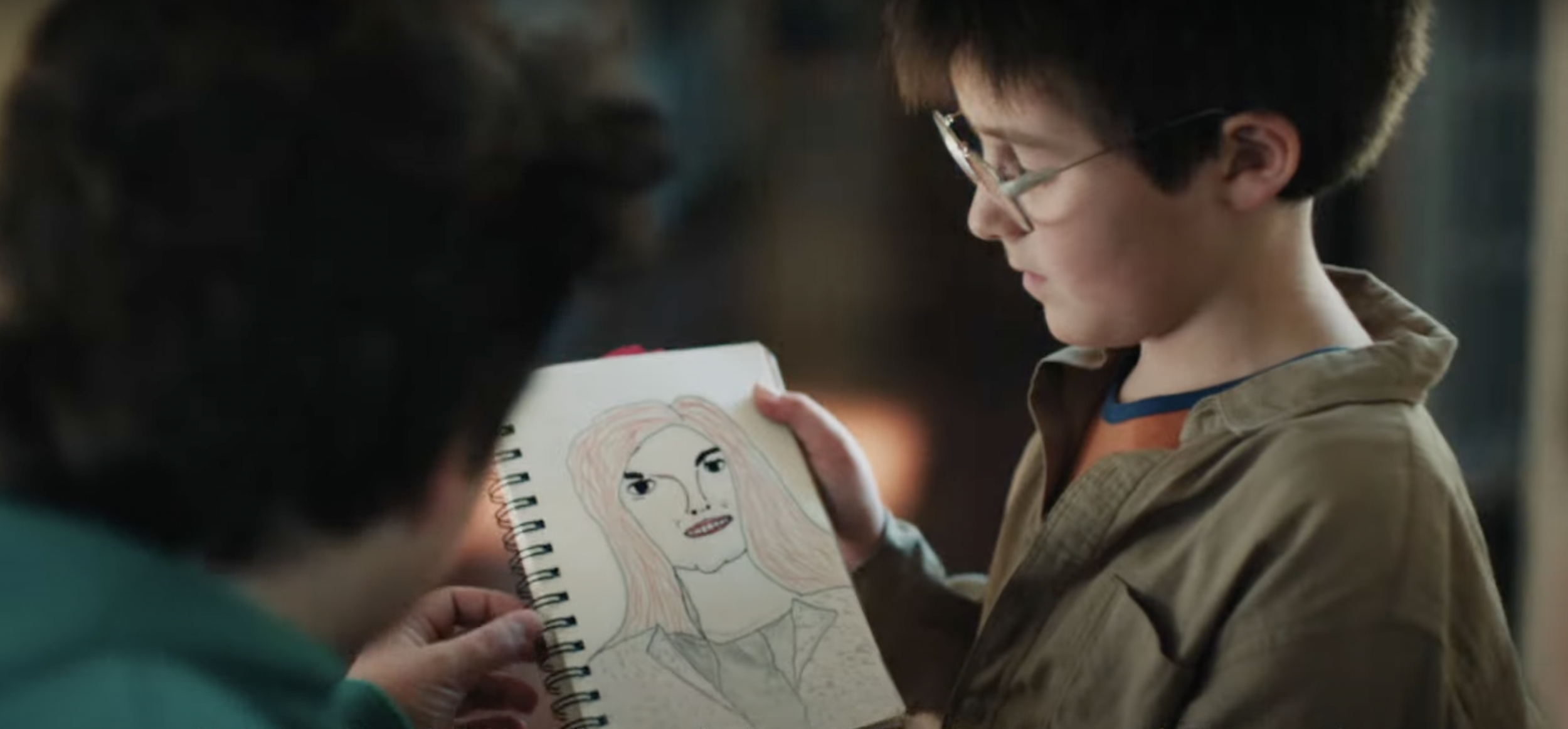 Un garçon montrant un croquis d'une personne avec des lunettes à un adulte.