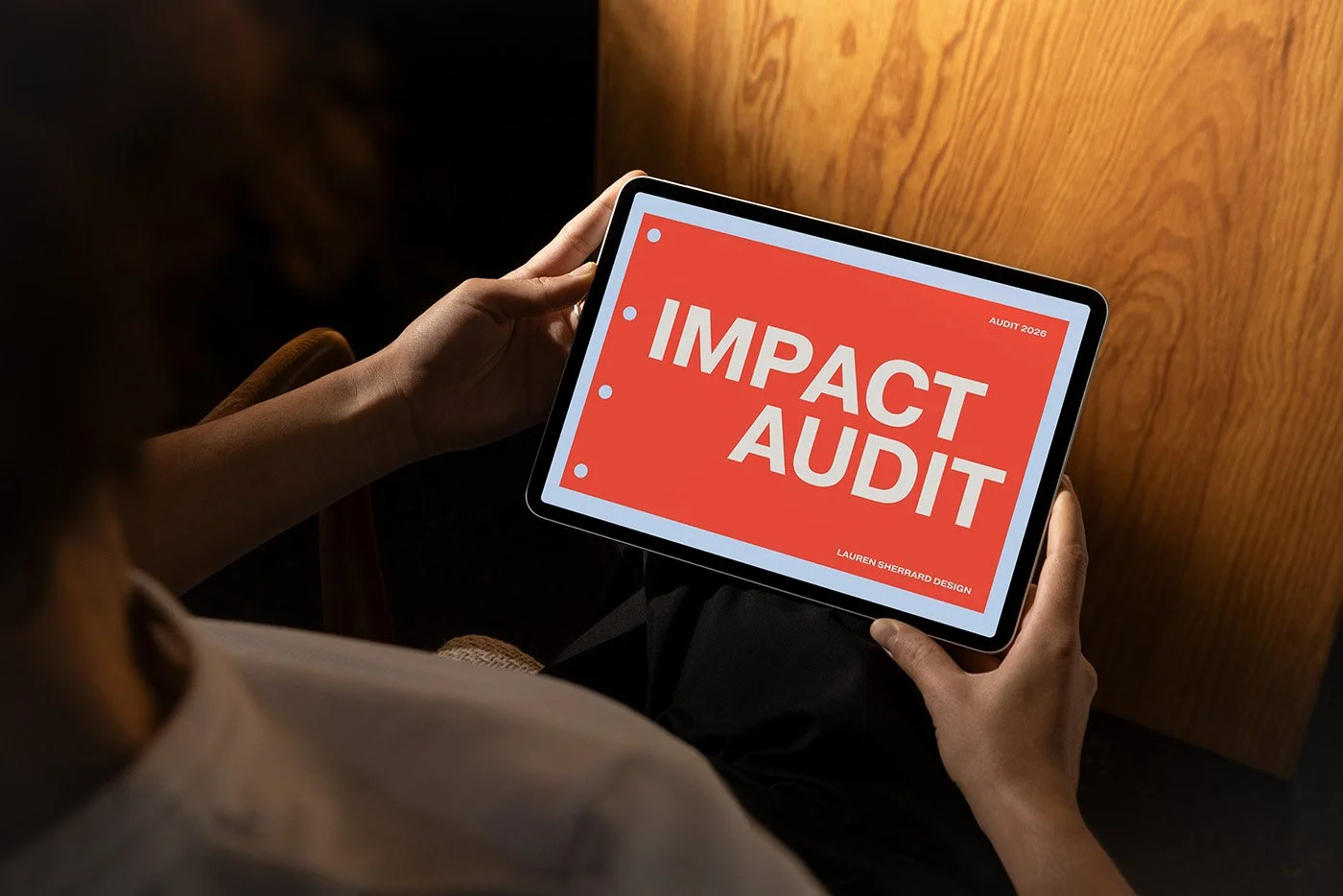 An ipad with the IMPACT audit cover apge on the front in large bold letters on a bright red background