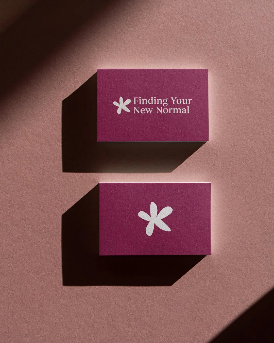 Business cards in the brand berry colour with the Finding Your New Normal logo