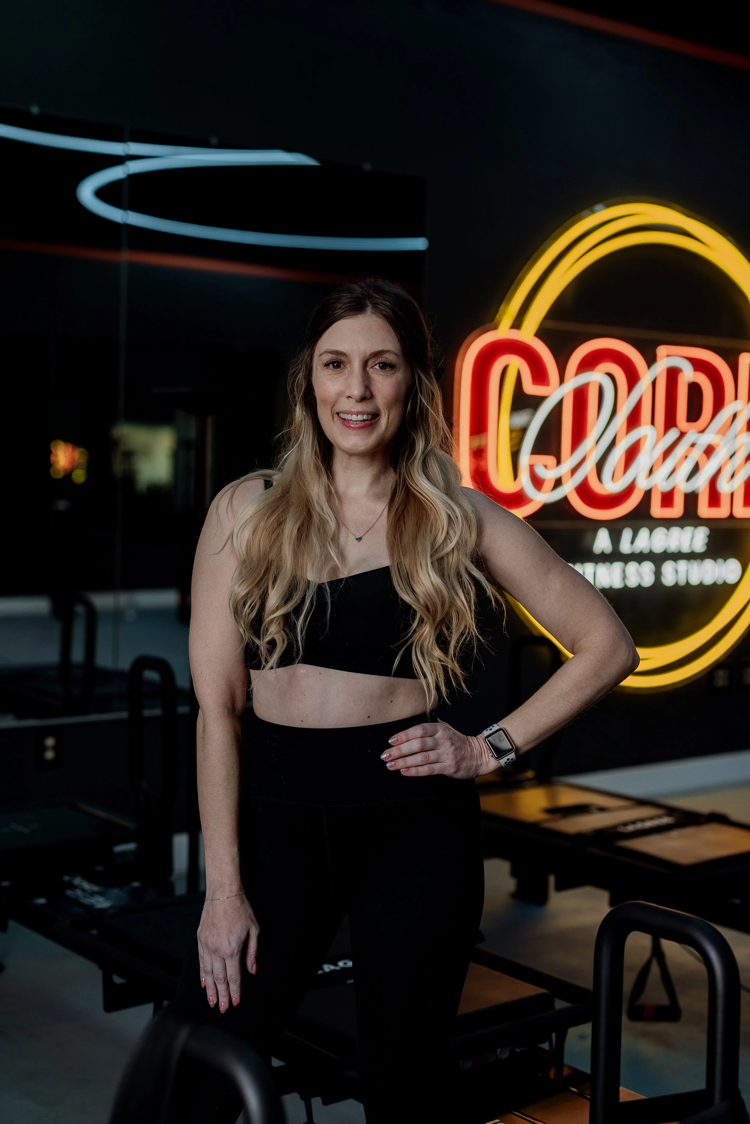 A woman in workout attire standing in a gym with neon signs in the background.
