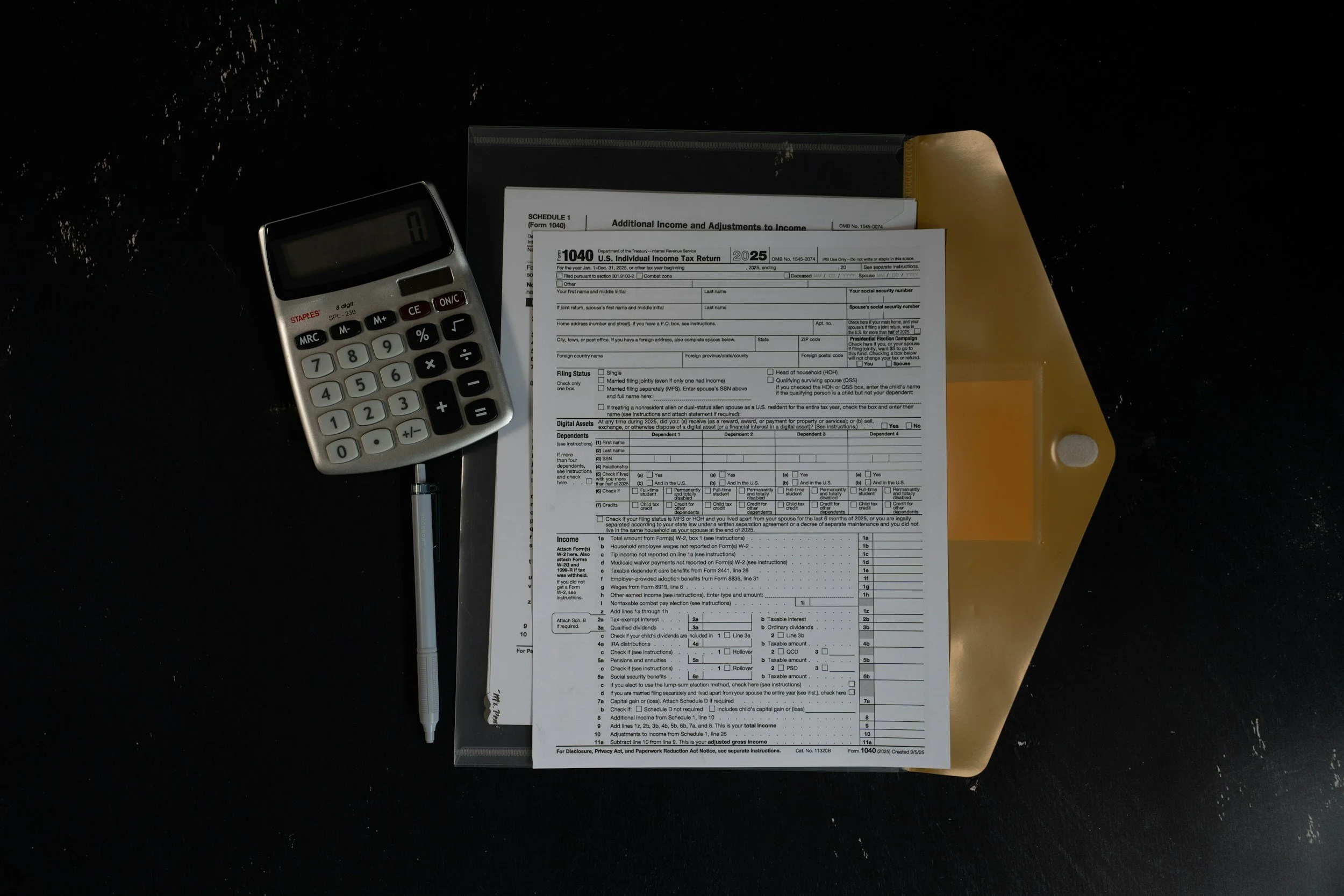 A calculator, a tax form, and a yellow folder on a black surface.