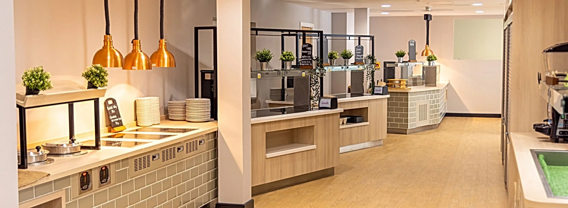 Empty buffet area with plates, potted plants, and condiment containers, with warm lighting and modern decor in a restaurant or hotel breakfast area.